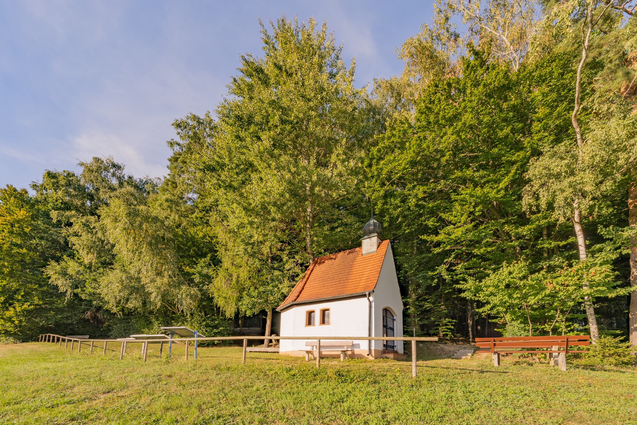 Bertenöder Kapelle in Stubenberg, Rottal-Inn, Niederbayern, Deutschland. Kapelle am Waldrand im Holzland. Grünfläche und Bäume mit Bank.