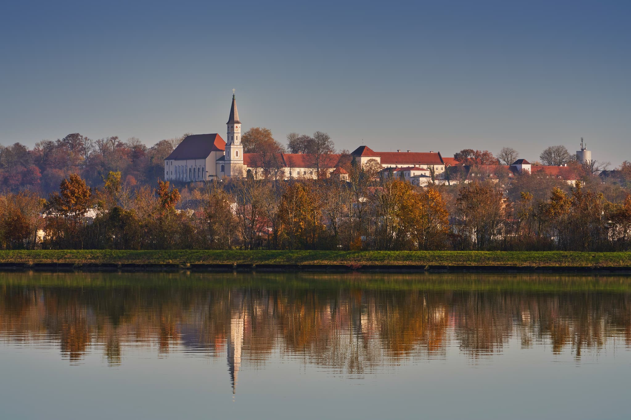 Aussicht nach Ranshofen von Kirchdorf am Inn, Rottal-Inn, Niederbayern. Der Fluss Inn spiegelt die herbstliche Landschaft unter klarem Himmel wider.