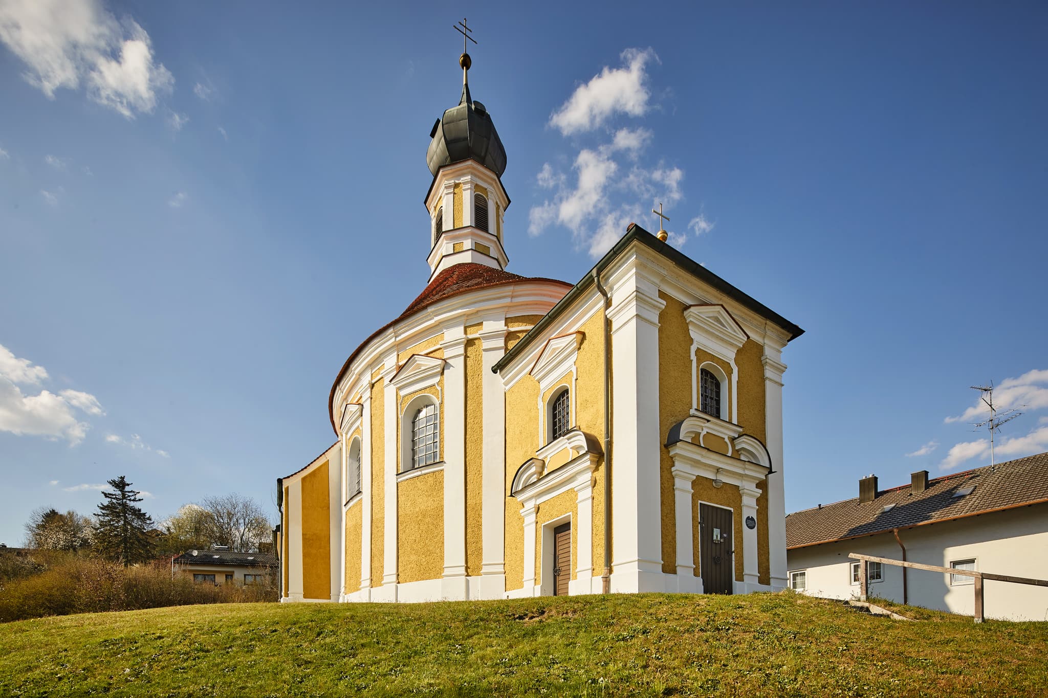 Die Filialkirche Sankt Antonius von Padua in Reischach, Altötting, Oberbayern, Deutschland. Ein historisches Gotteshaus auf einem Hügel unter blauem Himmel.
