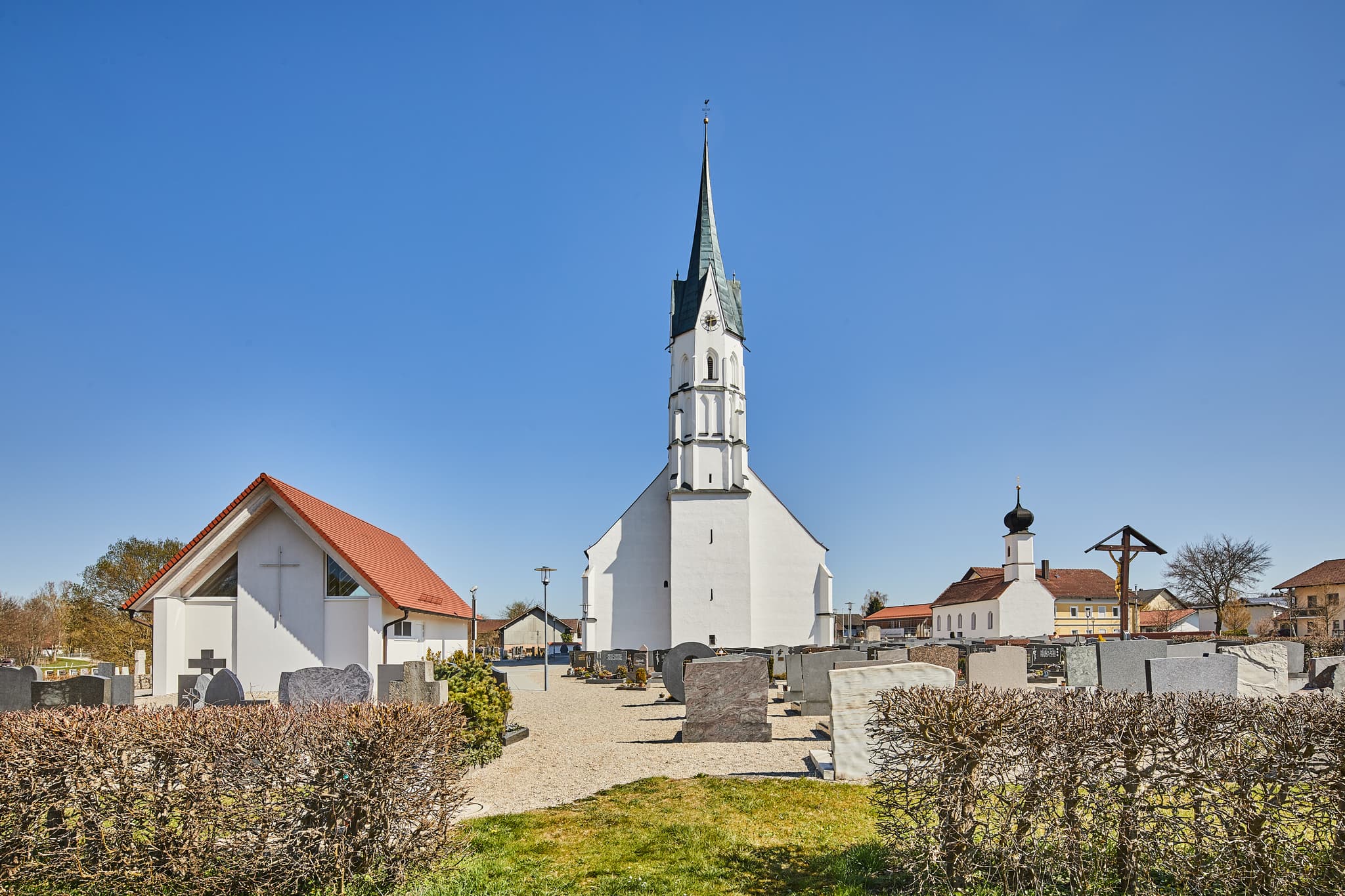 Pfarrkirche Mariä Heimsuchung in Unterdietfurt, Landkreis Rottal-Inn, Niederbayern, Deutschland. Holzland mit Kirche und Friedhof bei klarem Himmel.