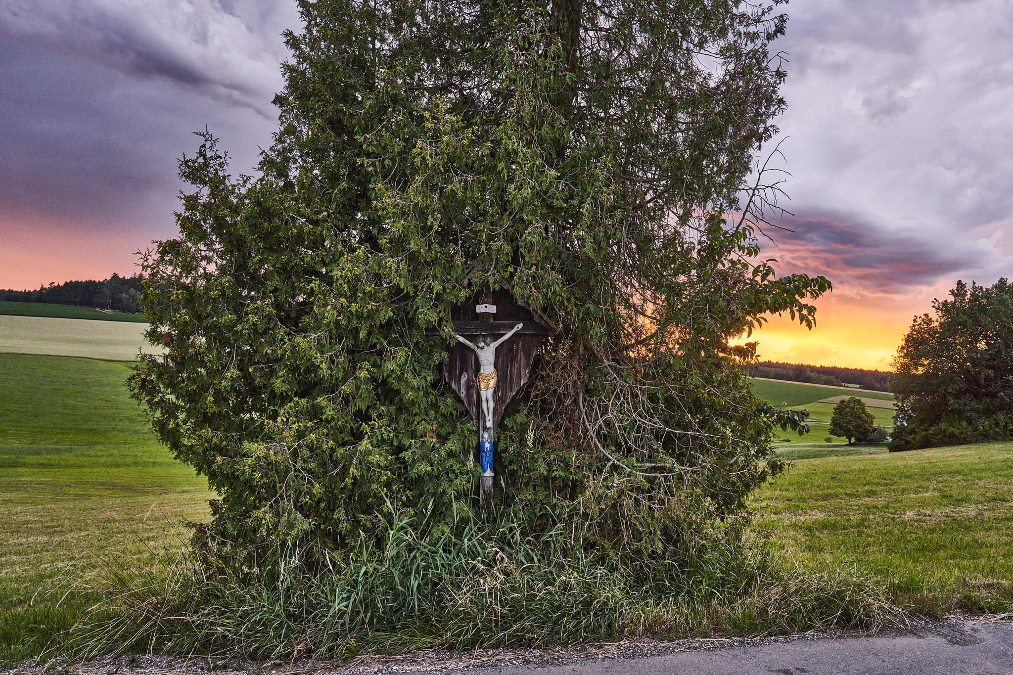 Ein Wegkreuz an einem Feldweg nahe Weiher in Arbing, Reischach, Landkreis Altötting, Oberbayern. Die Inn-Salzach Region in Deutschland bei Abendrot.