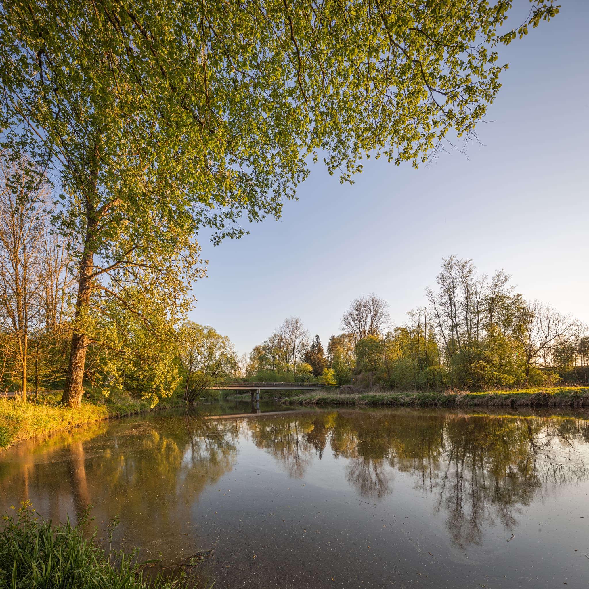 Idyllisches Panorama von Aufham Isen in Winhöring, Landkreis Altötting, Oberbayern. Die Region Inn-Salzach mit ruhigem Gewässer, Bäumen und Brücke.