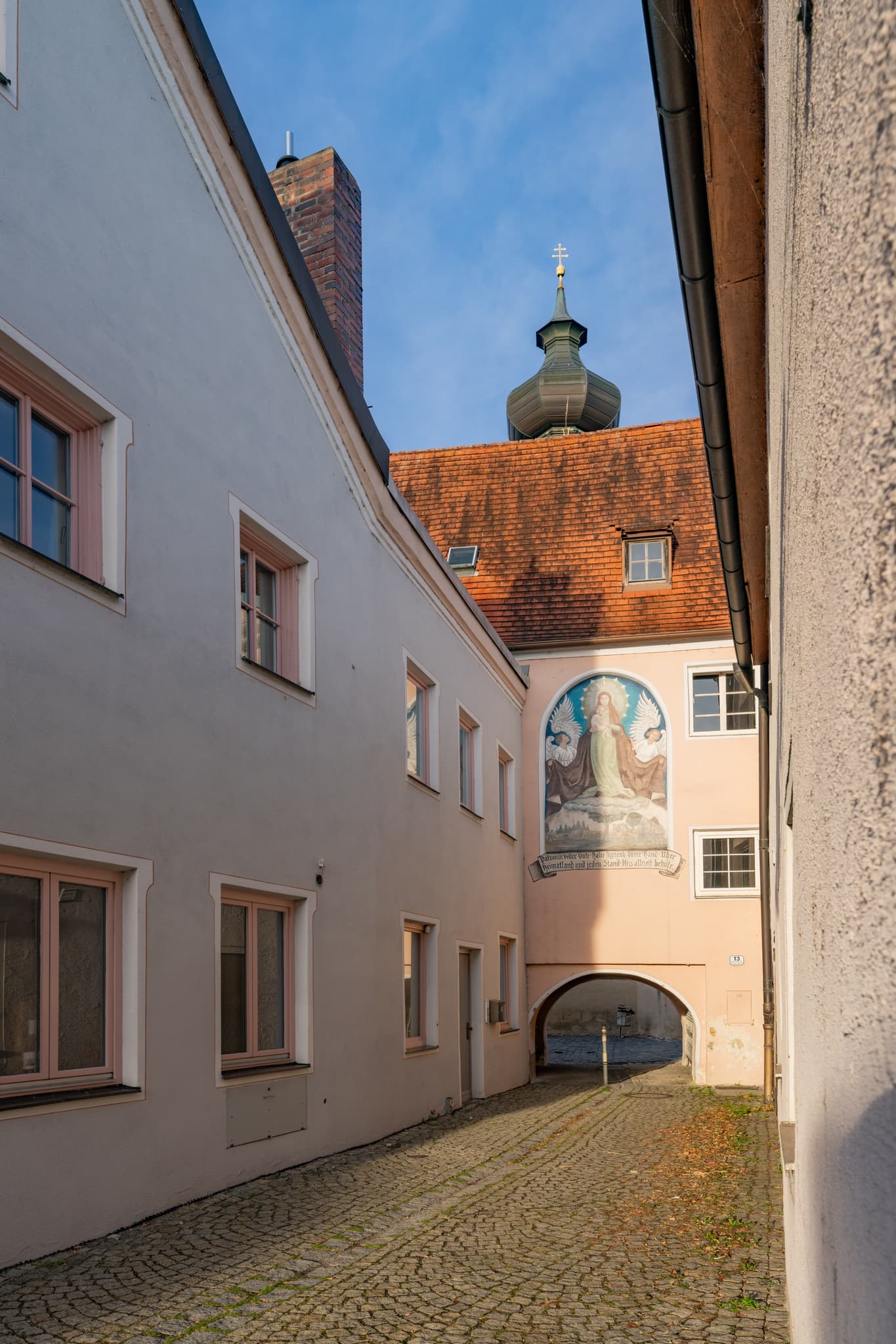 Gasse mit Tor zur Pfarrkirche St. Stephanus in Triftern, Rottal-Inn, Niederbayern, Bäderdreieck, Bayern. Durchgang zwischen Gebäuden mit Blick auf die Kirche.