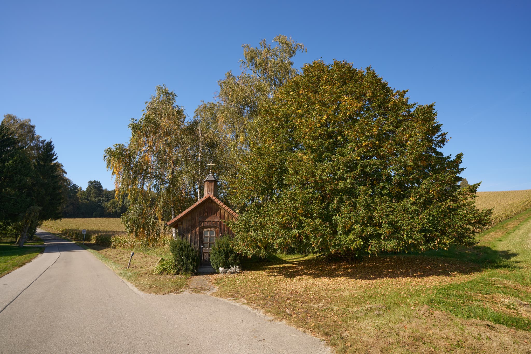 Holzkapelle in Stadlreith, Tettenweis, Landkreis Passau, Niederbayern. Im Donau-Wald, Deutschland, umgeben von Feldern und Bäumen bei blauem Himmel.