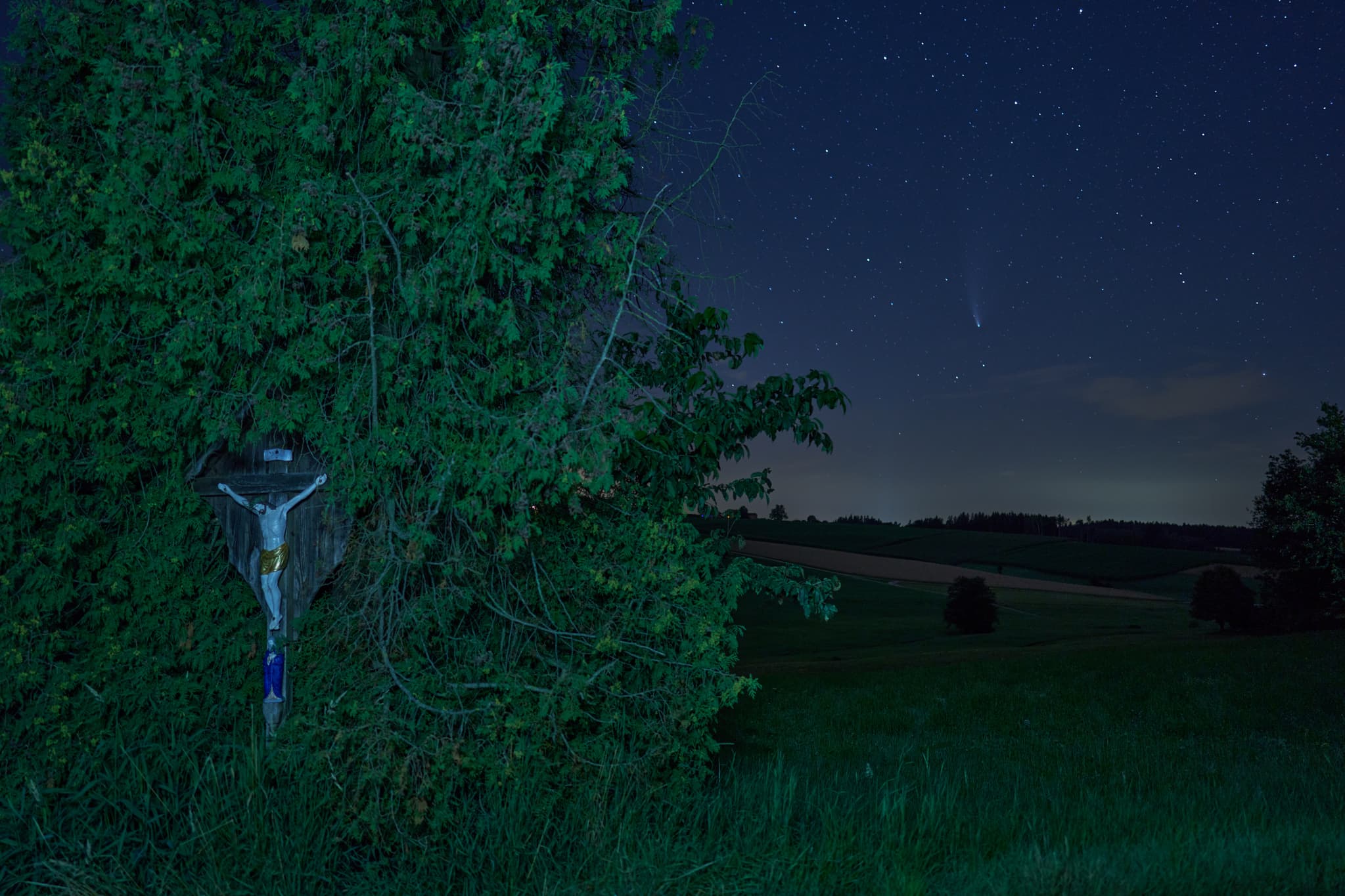 Nachtaufnahme Feldkreuz bei Arbing, Reischach, Landkreis Altötting, Oberbayern. Der Komet Neowise leuchtet am Sternenhimmel über der Landschaft im Holzland.