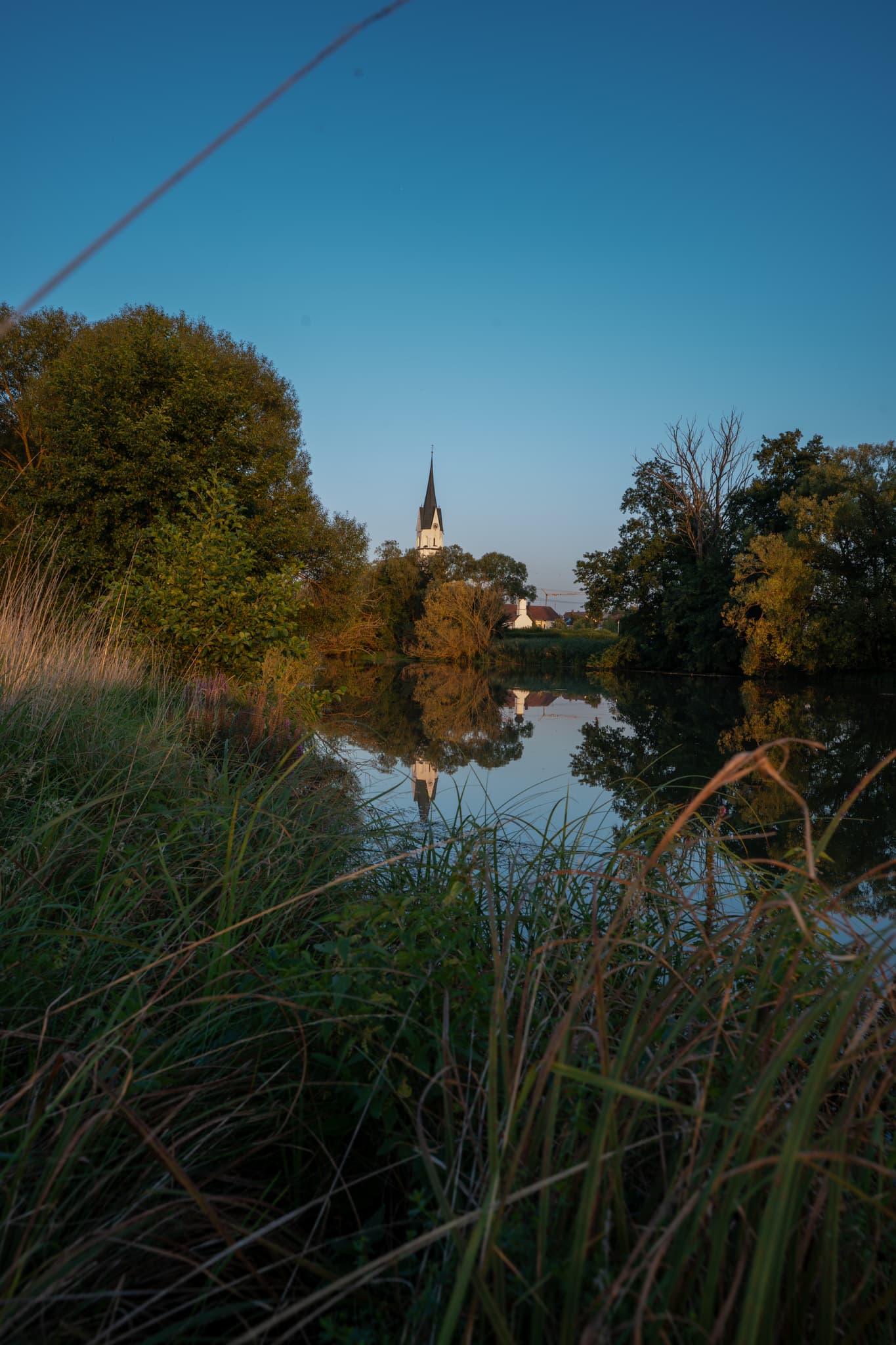 Friedliche Abendstimmung in Unterdietfurt. Der Kirchturm spiegelt sich in ruhigen Wasser,Warme Farben und weiches Licht erzeugen eine beschauliche Atmosphäre