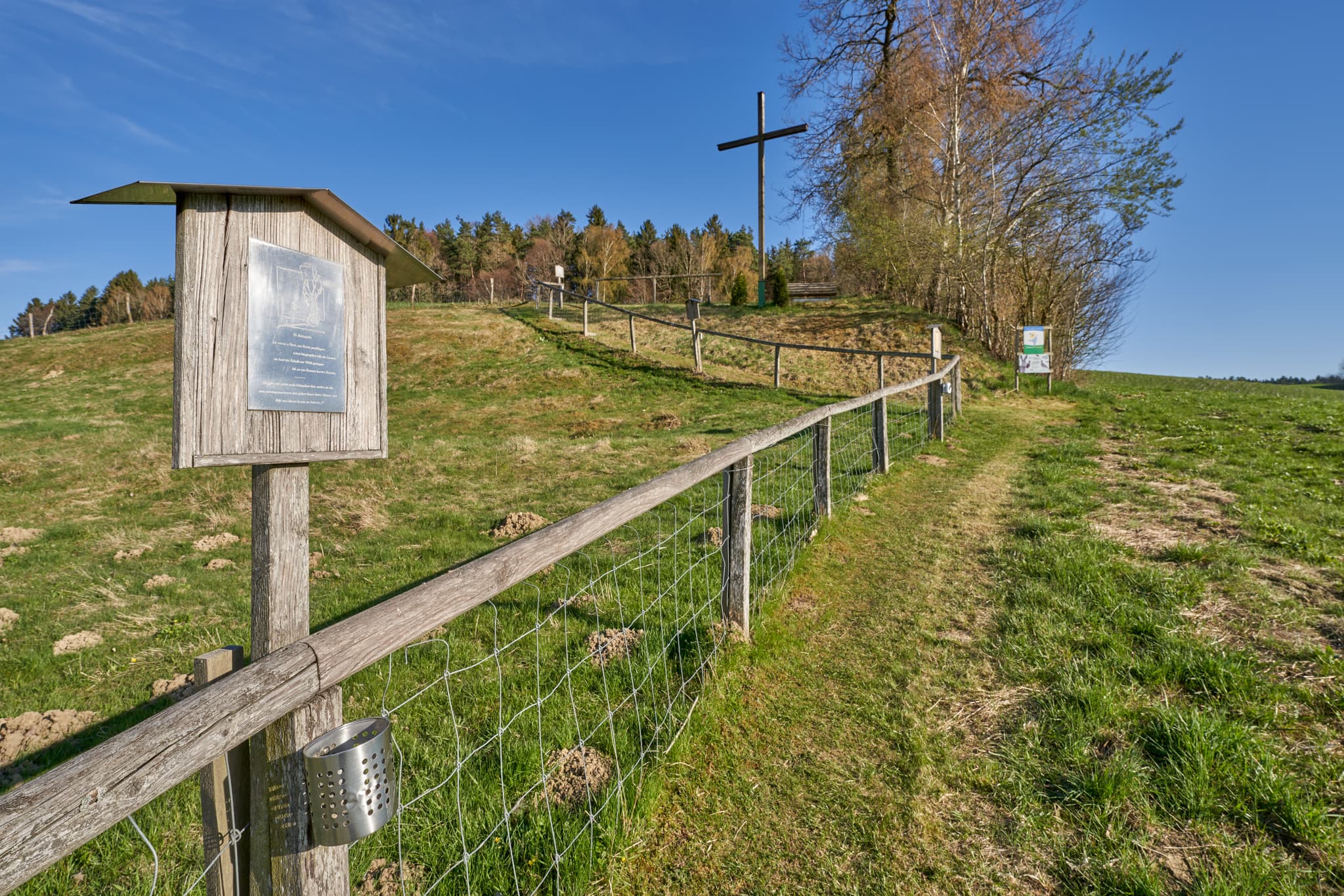 Kreuzweg Stationstafel und Holzkreuz auf Anhöhe in Erlbach, Landkreis Altötting, Oberbayern, Inn-Salzach, Deutschland. Feldweg und grüne Landschaft.