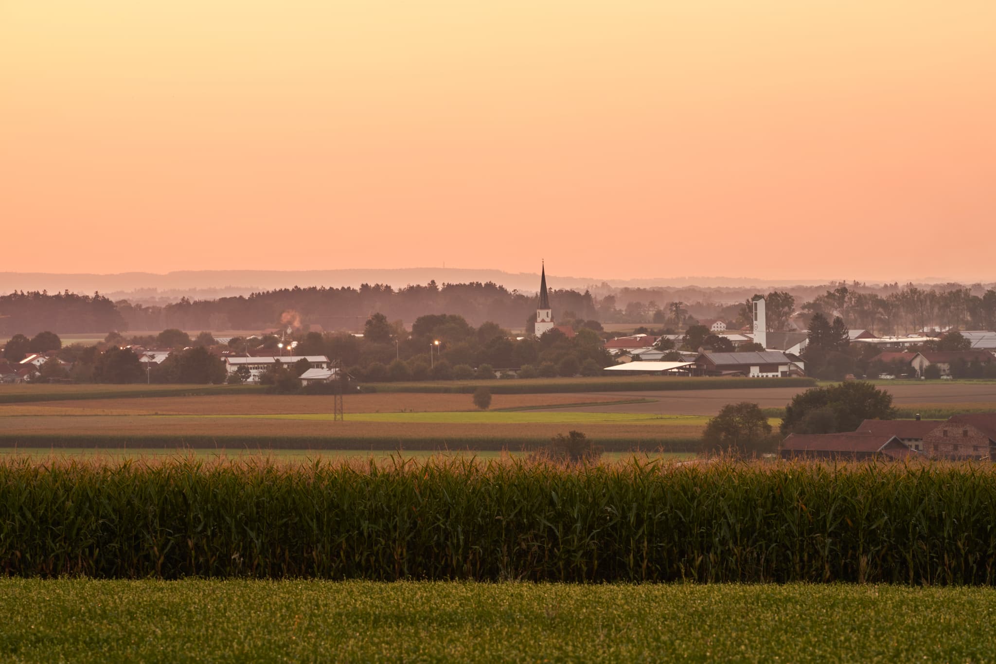 Blick von Oberschroffen auf die Landschaft Unterneukirchens im Landkreis Altötting, Oberbayern. Abenddämmerung über Feldern und Dorf in der Inn-Salzach Region.