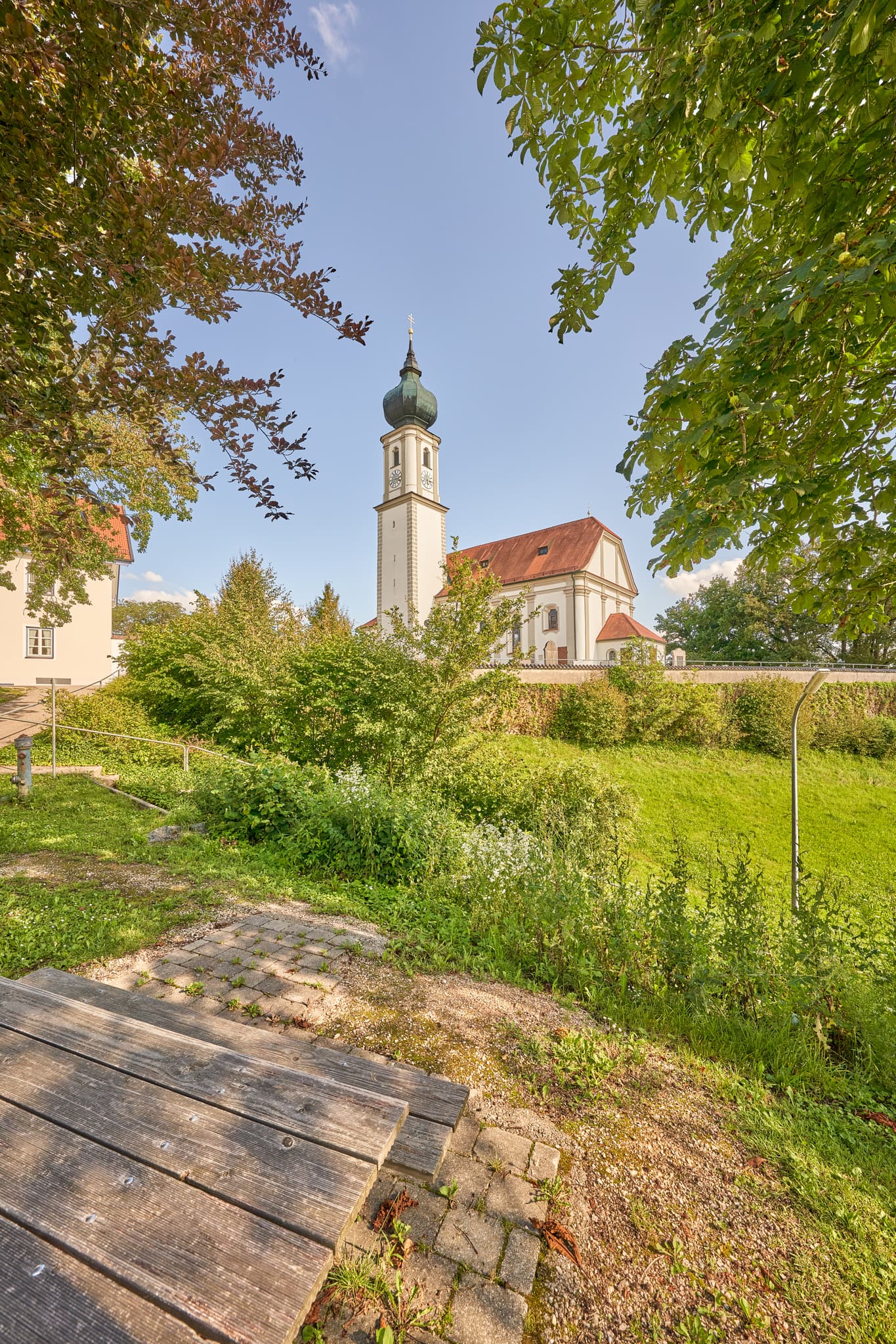 Kirche St. Martin, Niedertaufkirchen, Mühldorf am Inn, Oberbayern, Inn-Salzach. Historisches Gotteshaus mit Zwiebelturm und Mauer. Grüne Wiese, blauer Himmel.
