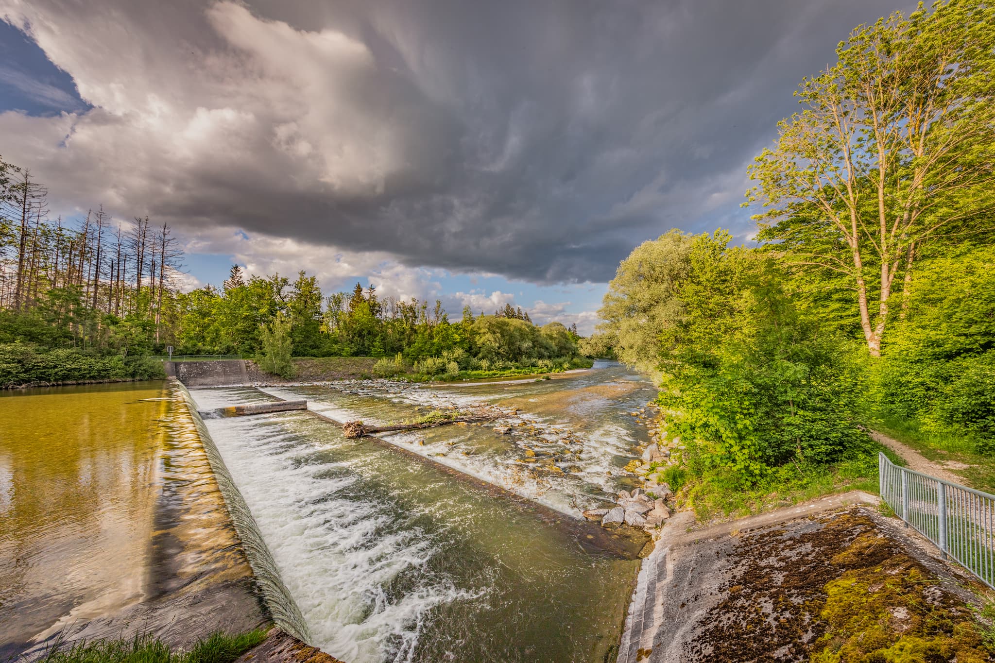 Flusslandschaft mit Wehr am Wald an der Alz bei Garching, Altötting, Oberbayern. Grüne Ufer und bewölkter Himmel im Inn-Salzach, Deutschland.