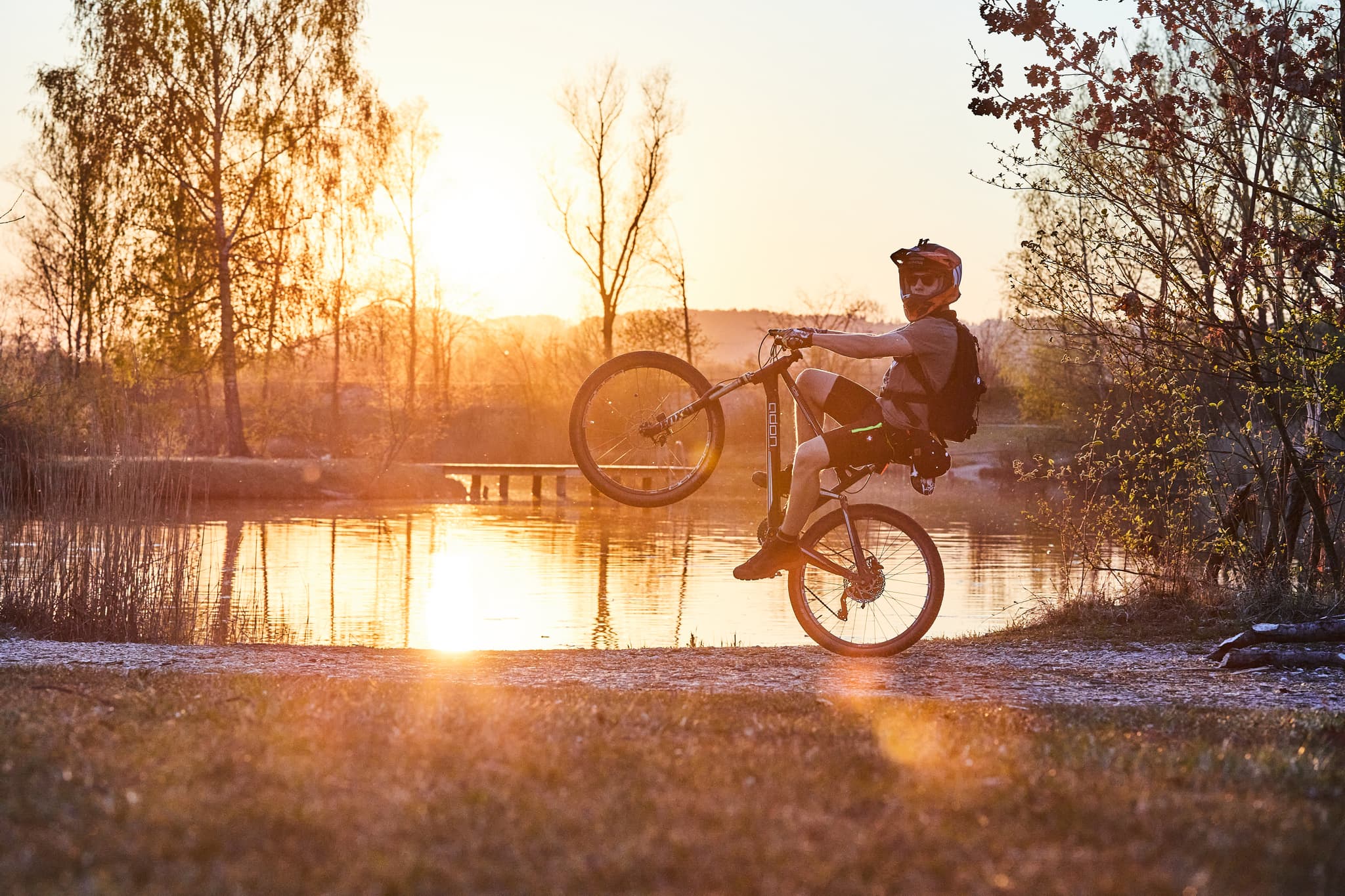 Ein Mountainbiker zeigt sein Können am malerischen Badesee Perach. Die abendliche Szene ist im Landkreis Altötting, Oberbayern, Inn-Salzach, Deutschland.