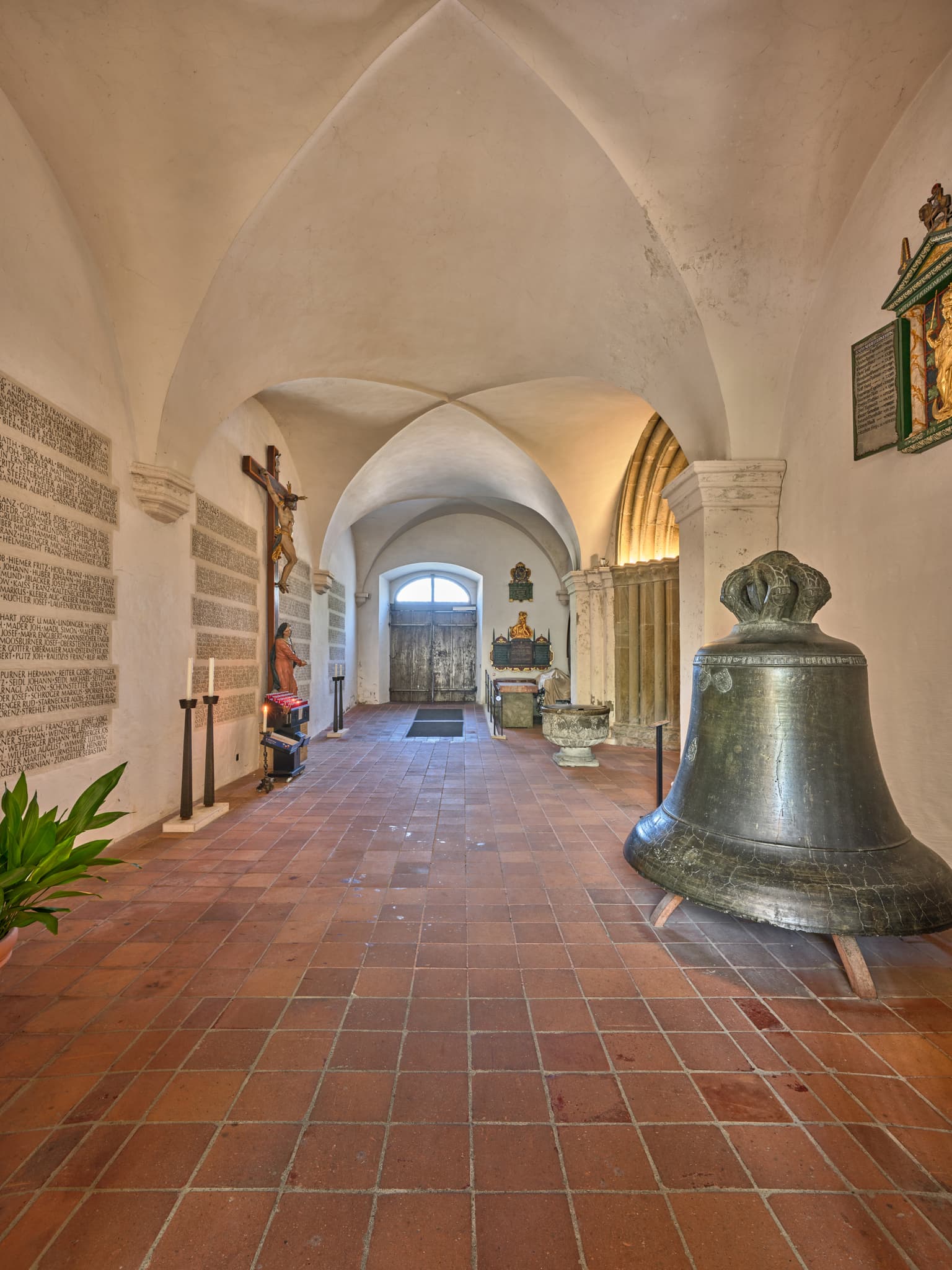 Historische Stiftskirche am Kapellplatz in Altötting, Oberbayern, Inn-Salzach, Deutschland. Zeigt Gewölbe, Fliesenboden, Kruzifix und eine große Glocke.