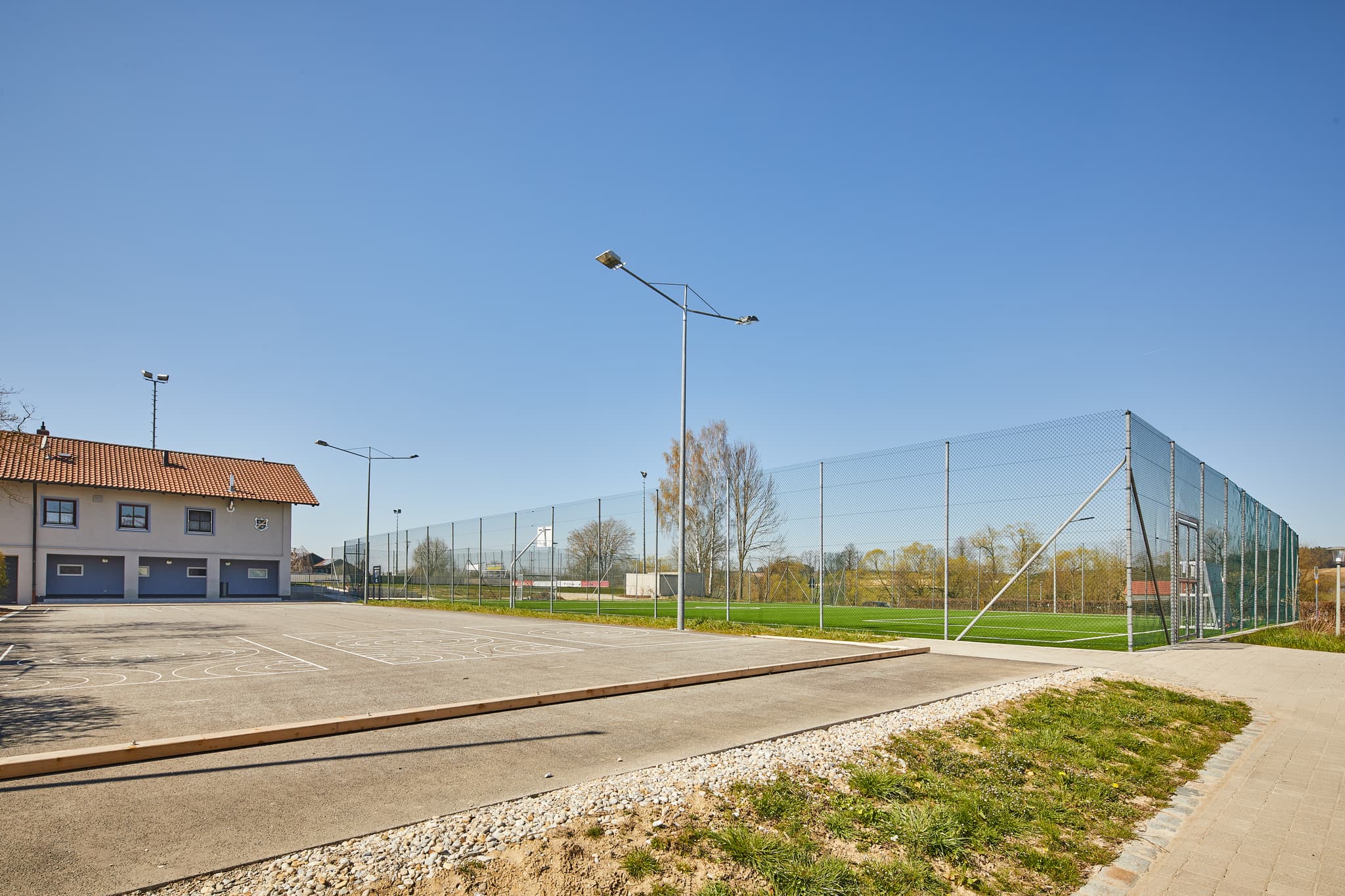 Sportanlage Unterdietfurt, Rottal-Inn, Niederbayern. Blick auf Sportfeld, asphaltierten Platz, Gebäude. Gelegen im Holzland, Deutschland, unter blauem Himmel.