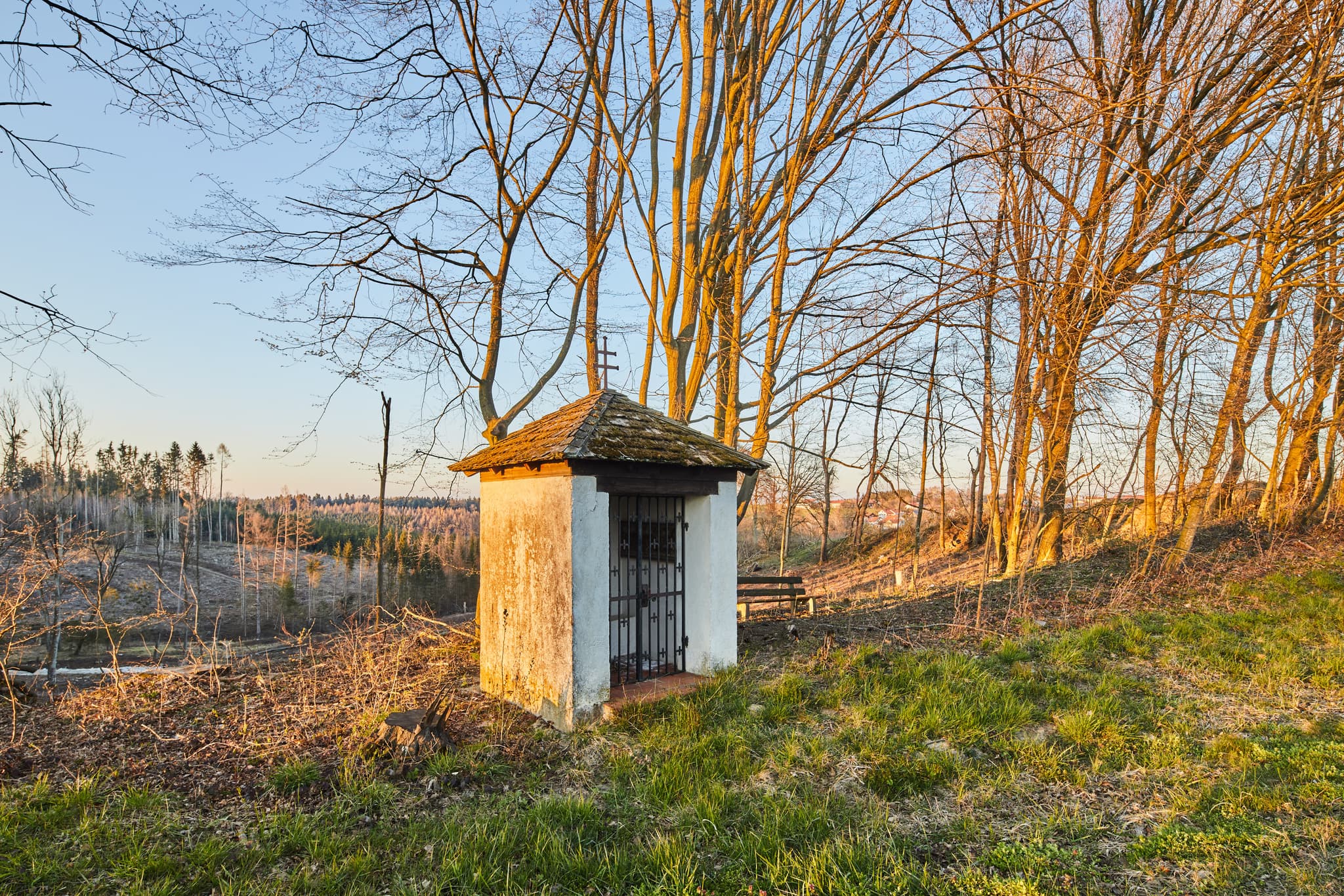 Bildstock mit Bank am Ortseingang von Wurmannsquick im Landkreis Rottal-Inn, Niederbayern, Deutschland. Ländliche Waldlandschaft im Holzland.