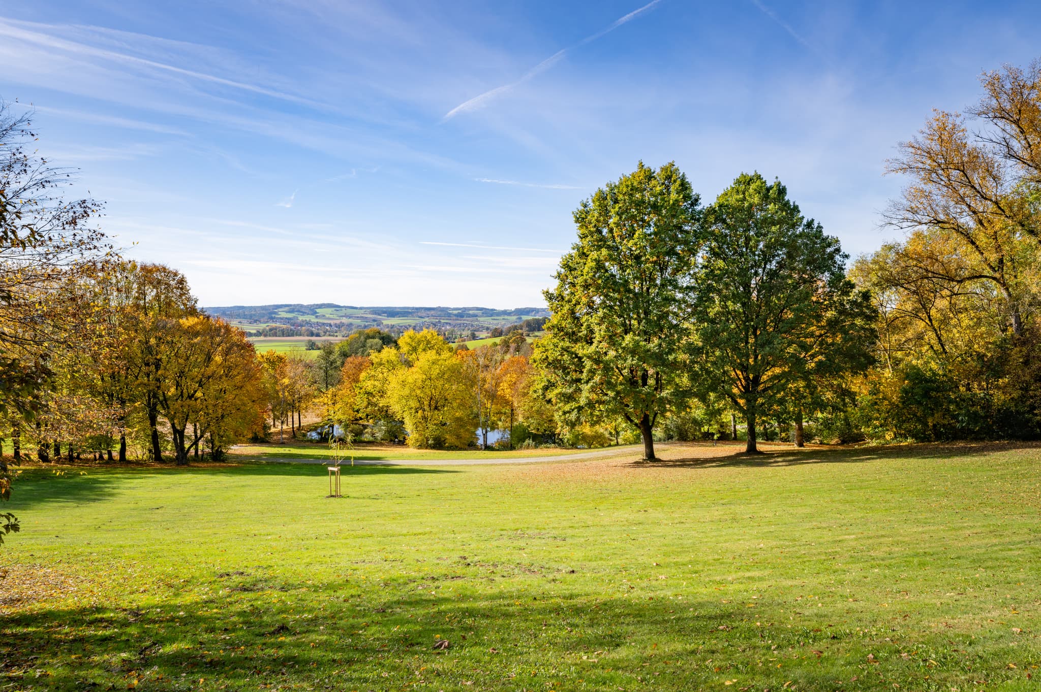 Herbst im Kurpark Bad Griesbach im Rottal. Bunte Bäume und weite Wiesen in Niederbayern, Deutschland. Erholsames Ambiente bei optimalem Wetter.