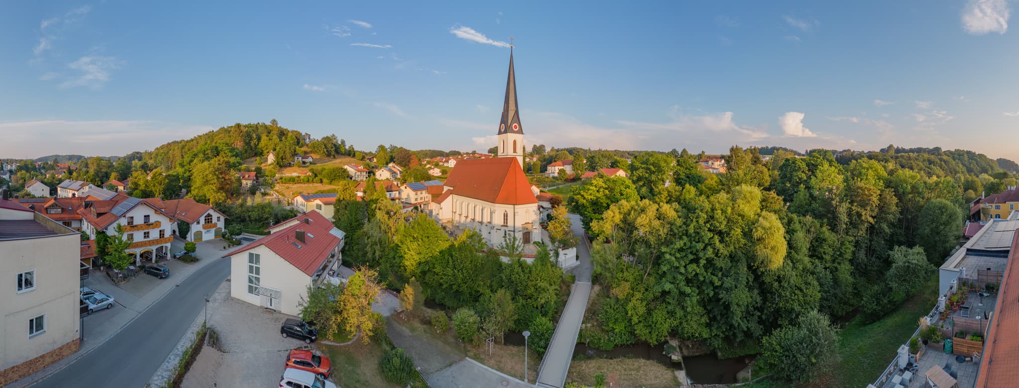 Der Reischachbach, Altötting, Oberbayern, hinter dem Rathaus. Im Hintergrund der Kirchturm St. Martin, umgeben von dichtem Grün.