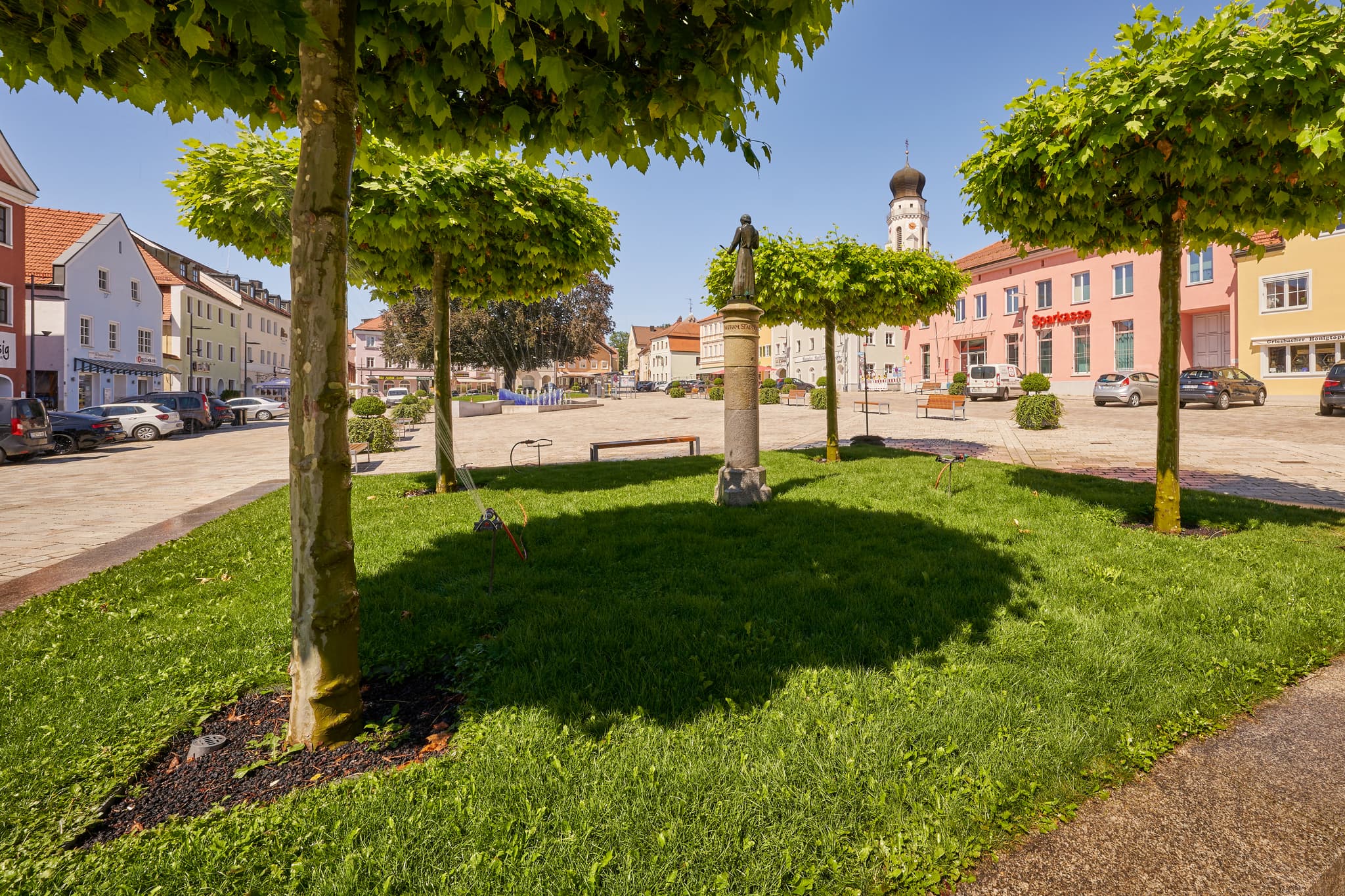 Blick auf den sonnigen Stadtplatz in Bad Griesbach im Landkreis Passau, Niederbayern, Deutschland. Platanen, Statue und historische Gebäude.