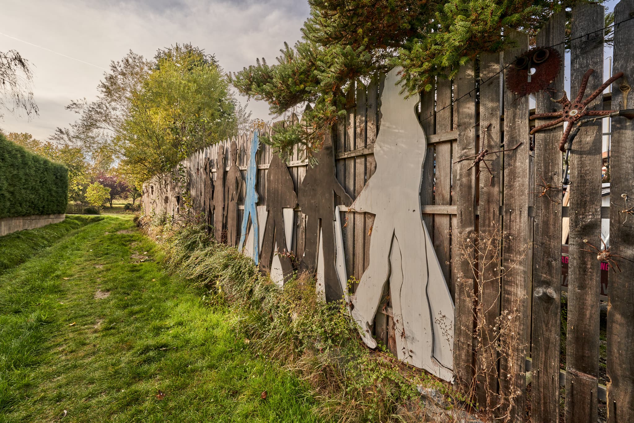 Rustikaler Zaun mit Figuren und Spinnen-Objekt am Feldweg in Schönau, Rottal-Inn, Niederbayern. Ländliche Umgebung im Holzland, Deutschland.