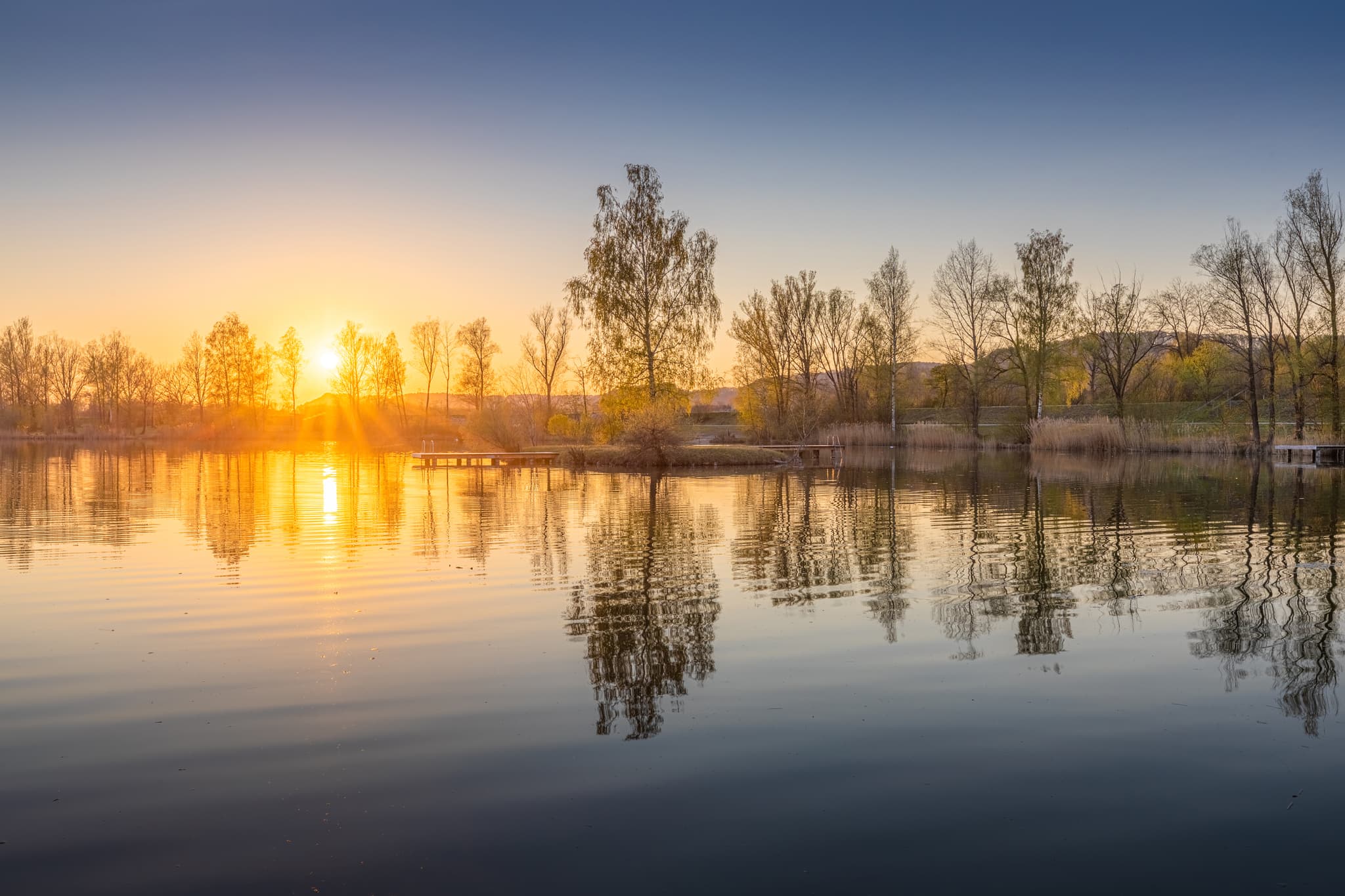 Idyllischer Badesee in Perach bei Sonnenuntergang. Oberbayern, Inn-Salzach Region, Deutschland. Herrliche Abendstimmung am See.