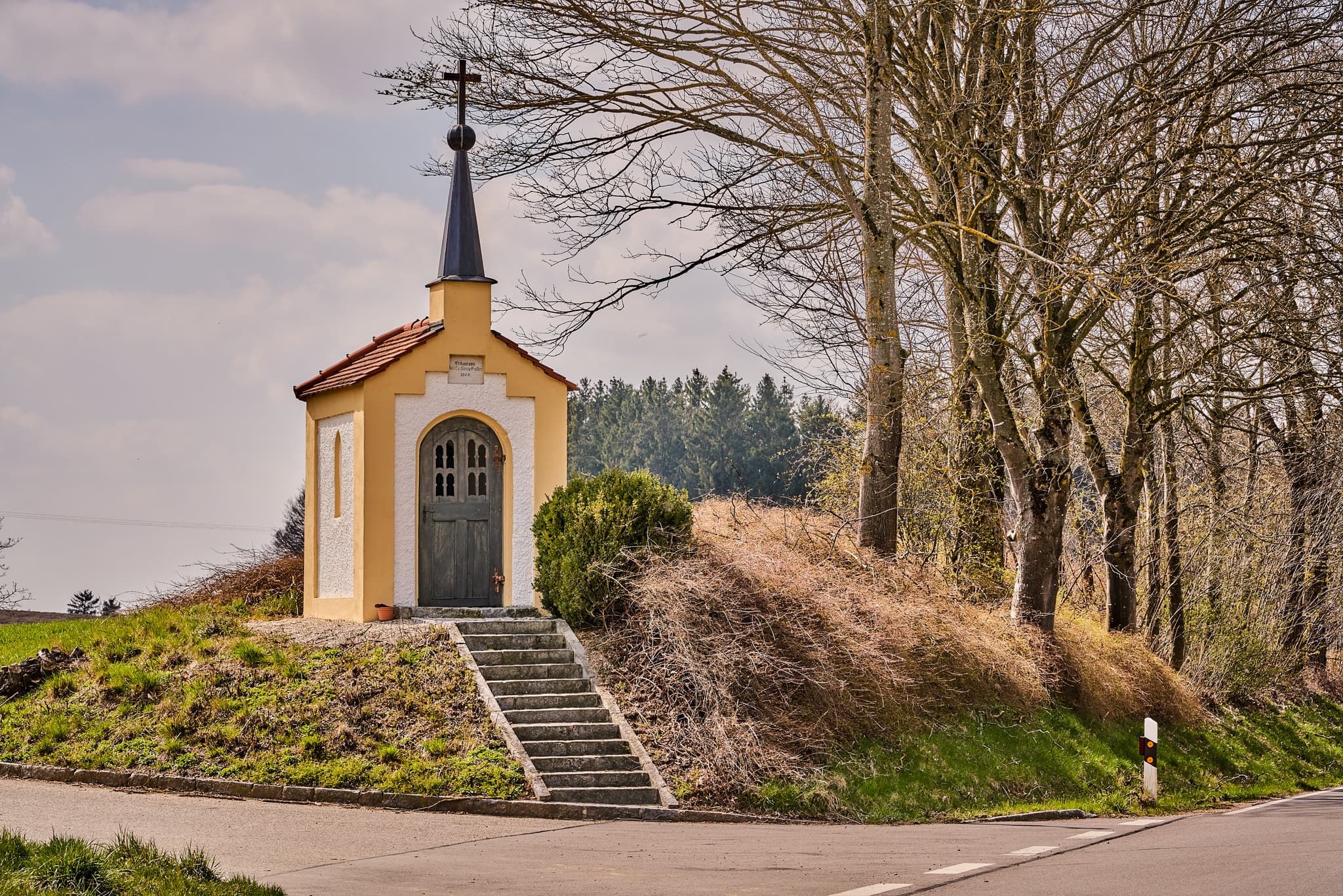 Kapelle in Rockersbach, Ortsteil Reischach, Altötting, Oberbayern. Bauwerk auf grasbewachsenem Hügel in der Region Inn-Salzach, Deutschland, umgeben von Bäumen.
