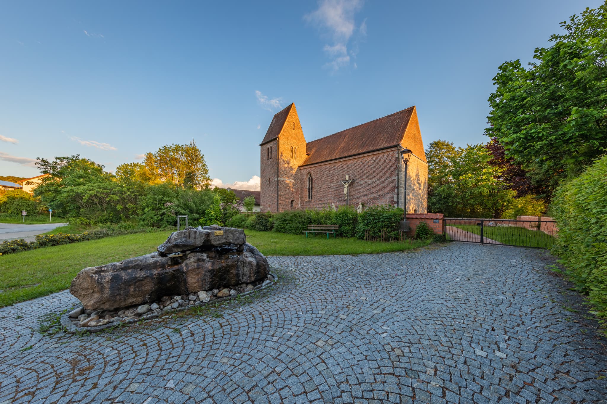 Filialkirche St. Rupert in Gumpersdorf, Zeilarn, Rottal-Inn, Niederbayern, Holzland, umgeben Grünflächen, Bäumen. Gepflasterter Vorplatz, Steinskulptur.