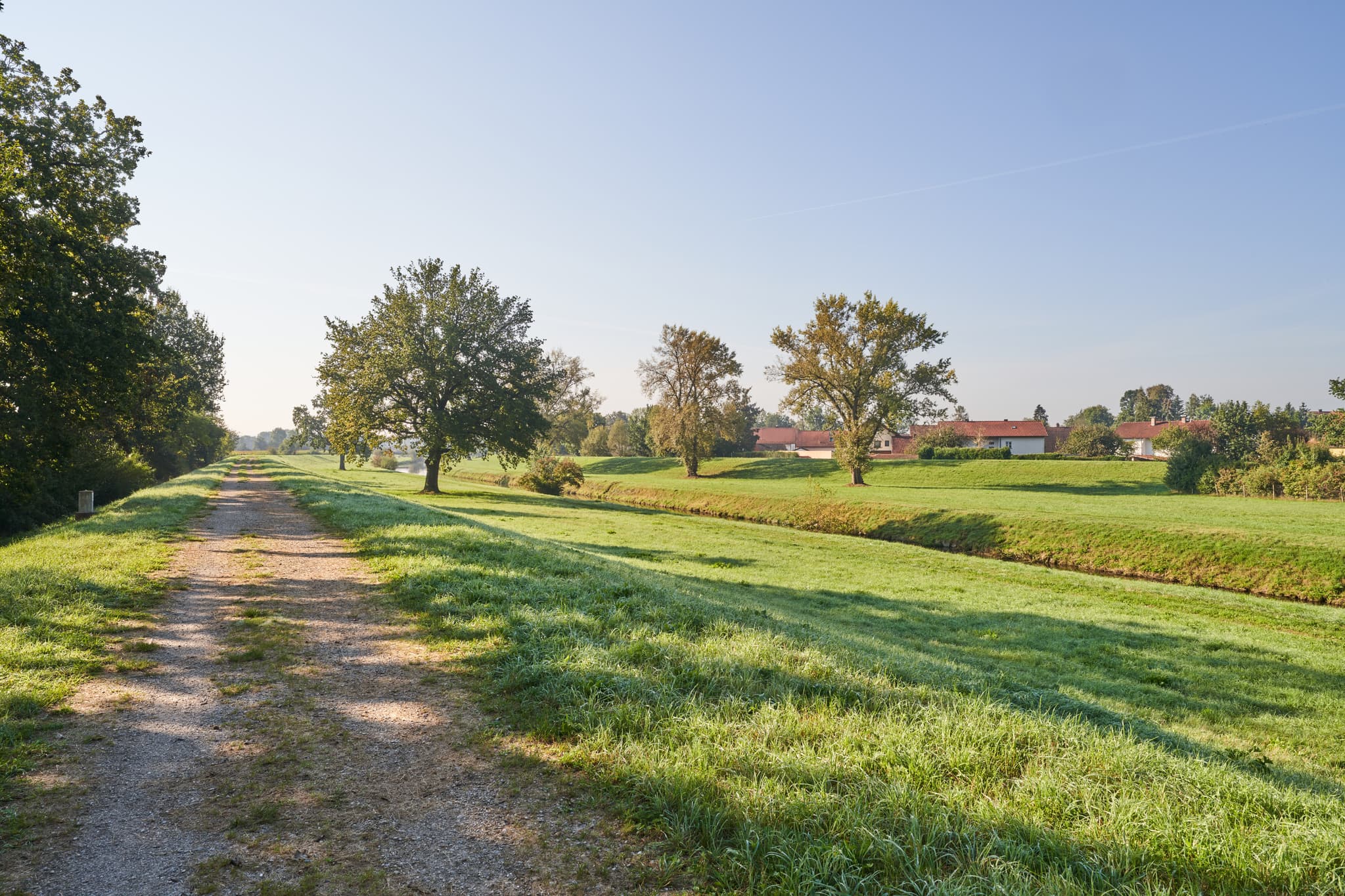 Feldweg durch Wiesen und Bäume mit Blick auf Steinhöring in Winhöring, Landkreis Altötting, Oberbayern. Die Landschaft der Region Inn-Salzach in Deutschland.