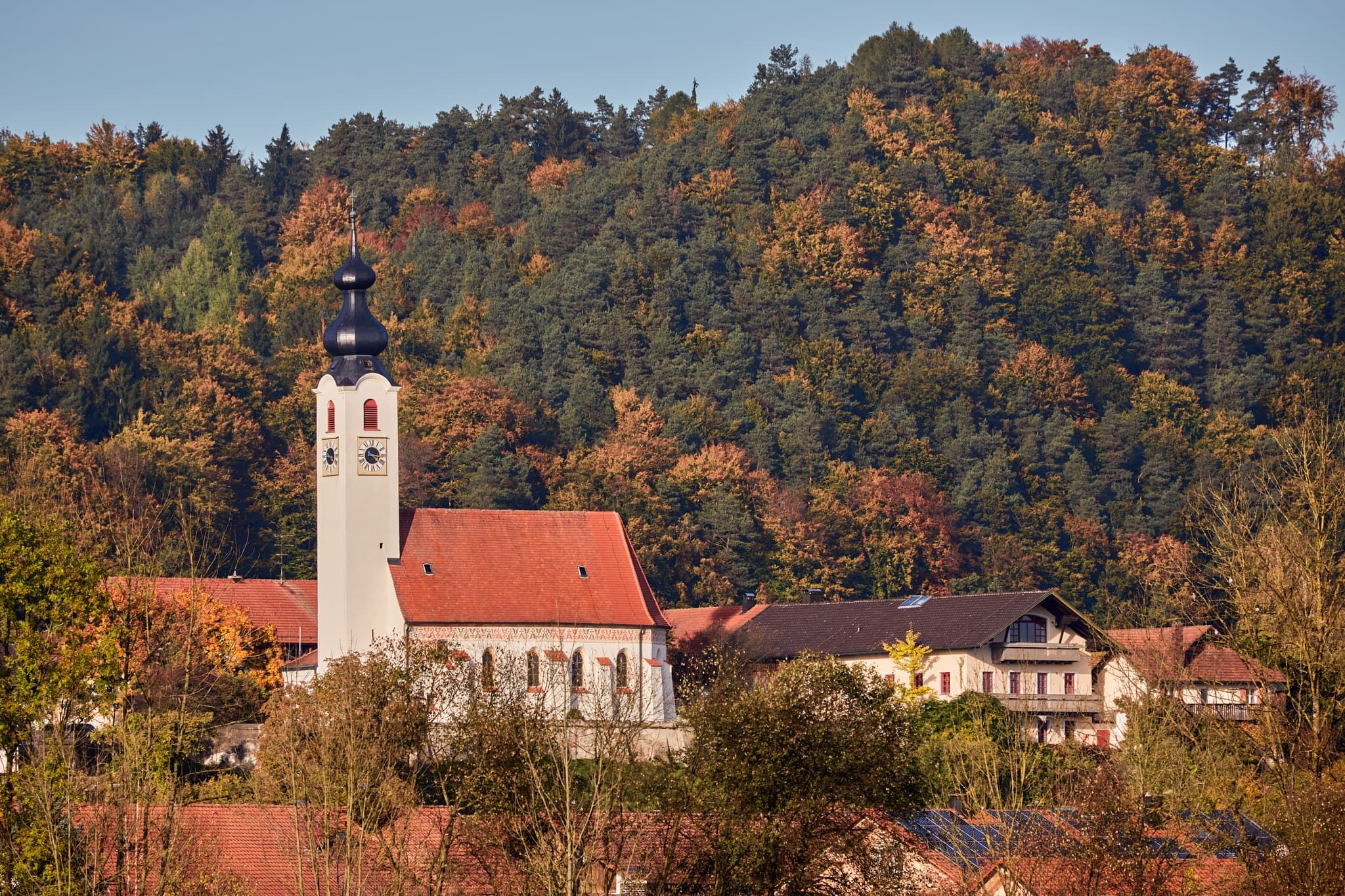 Blick vom Badesee Parkplatz nach  Perach, Landkreis Altötting, Oberbayern. Motiv zeigt lokale Architektur in der Landschaft der Region Inn-Salzach, Deutschland.