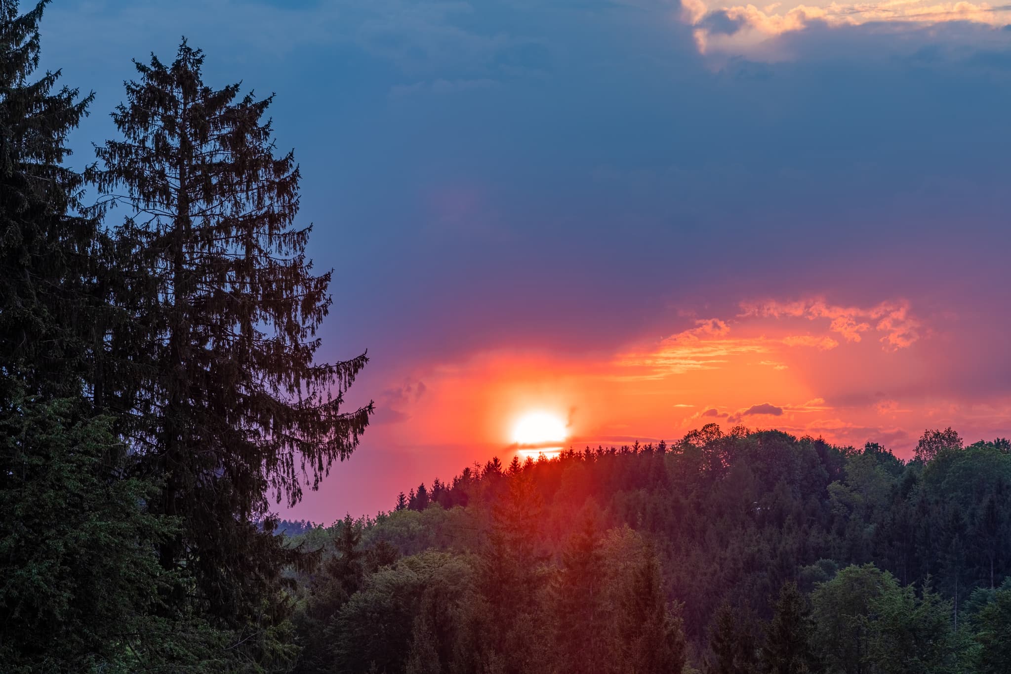 Ein Sonnenuntergang über der bewaldeten Hügellandschaft bei Mandelsberg, Winhöring, Altötting, Oberbayern, Region Inn-Salzach, Deutschland. Ruhiger Abendhimmel.