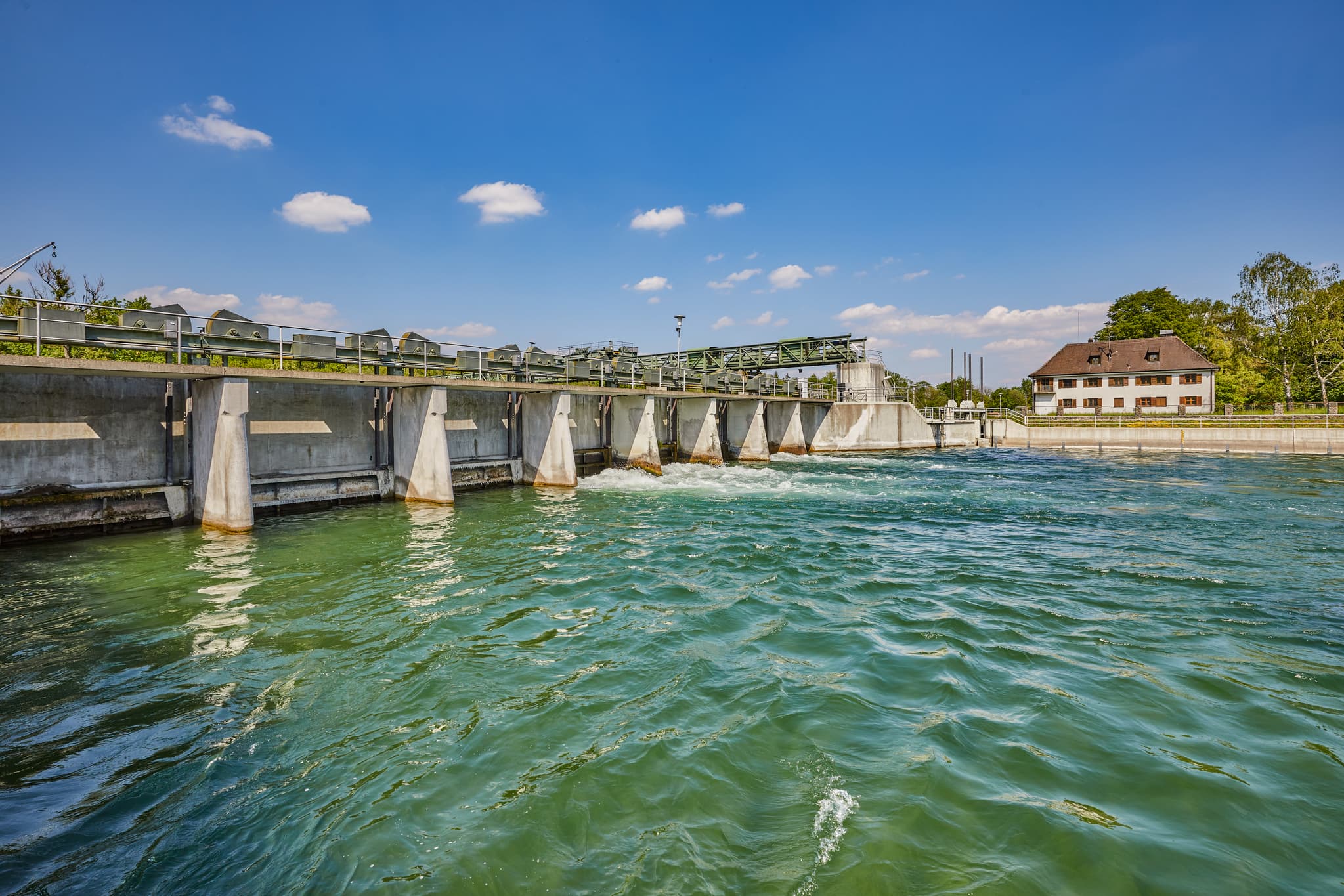 Wehranlage Alz, Burgkirchen-Hirten, Burgkirchen, Altötting, Oberbayern. Klares Wasser prägt Inn-Salzach, Deutschland. Betriebsgebäude, Uferbäume, blauer Himmel.