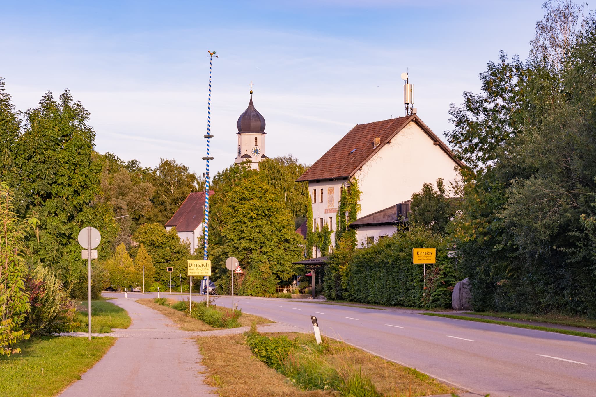 Ortseingang Dirnaich, Ortsteil Gangkofen, Landkreis Rottal-Inn, Niederbayern. Ansicht mit Maibaum, Kirchturm und bewaldeter Landschaft im Holzland, Deutschland.