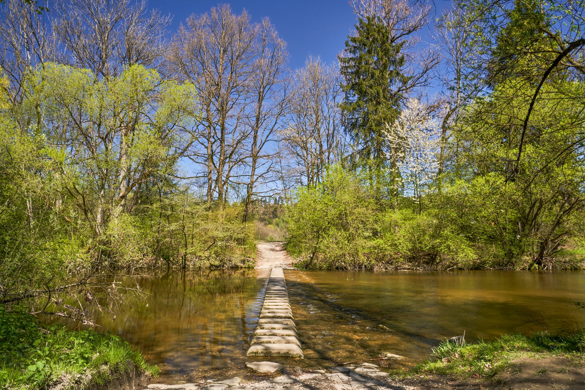 Trittsteine über Bach inmitten frühlingsgrüner Natur. Isen, Winhöring, Lkrs. Altötting, Oberbayern, Inn-Salzach, Deutschland. Ruhige Bachlandschaft.