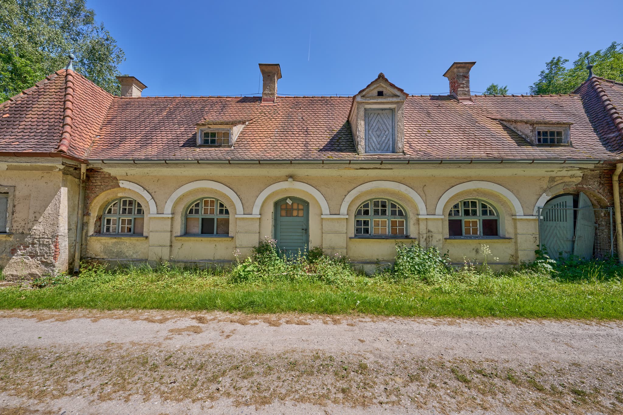 Alte Wäscherei Ecksberg, Mühldorf am Inn, Oberbayern. Historisches Gebäude der Region Inn-Salzach. Zeigt Rundbogenfenster, grüne Tür, üppige Vegetation.