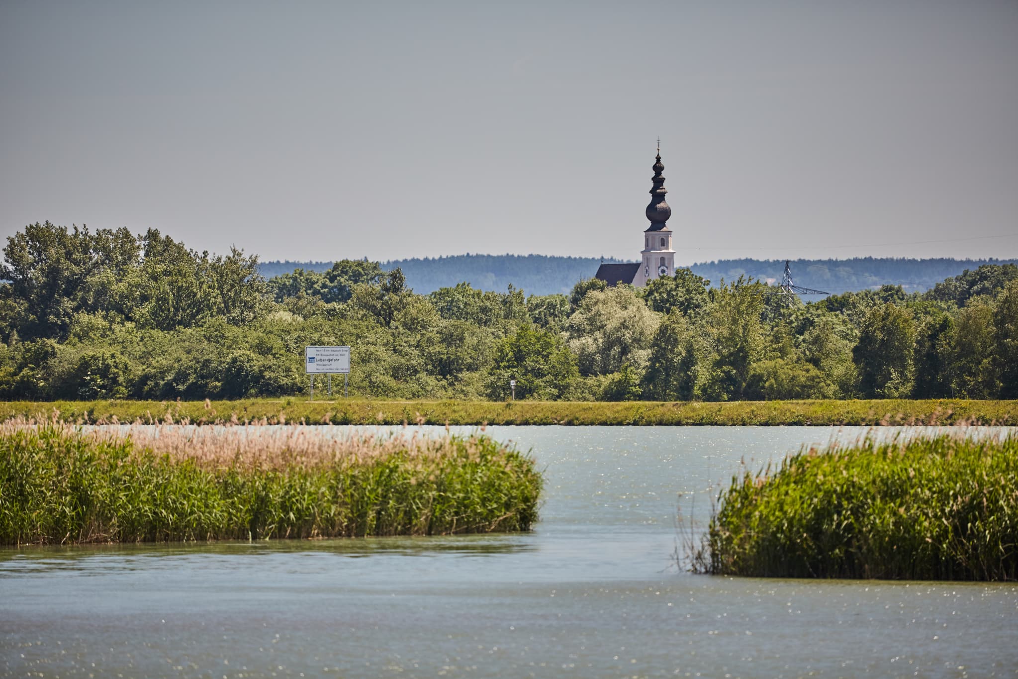 Panoramablick über den Inn bei Ering am Inn, Rottal-Inn, Niederbayern. Die Landschaft zeigt Fluss, Schilf, Bäume und die Kirche in Mining.