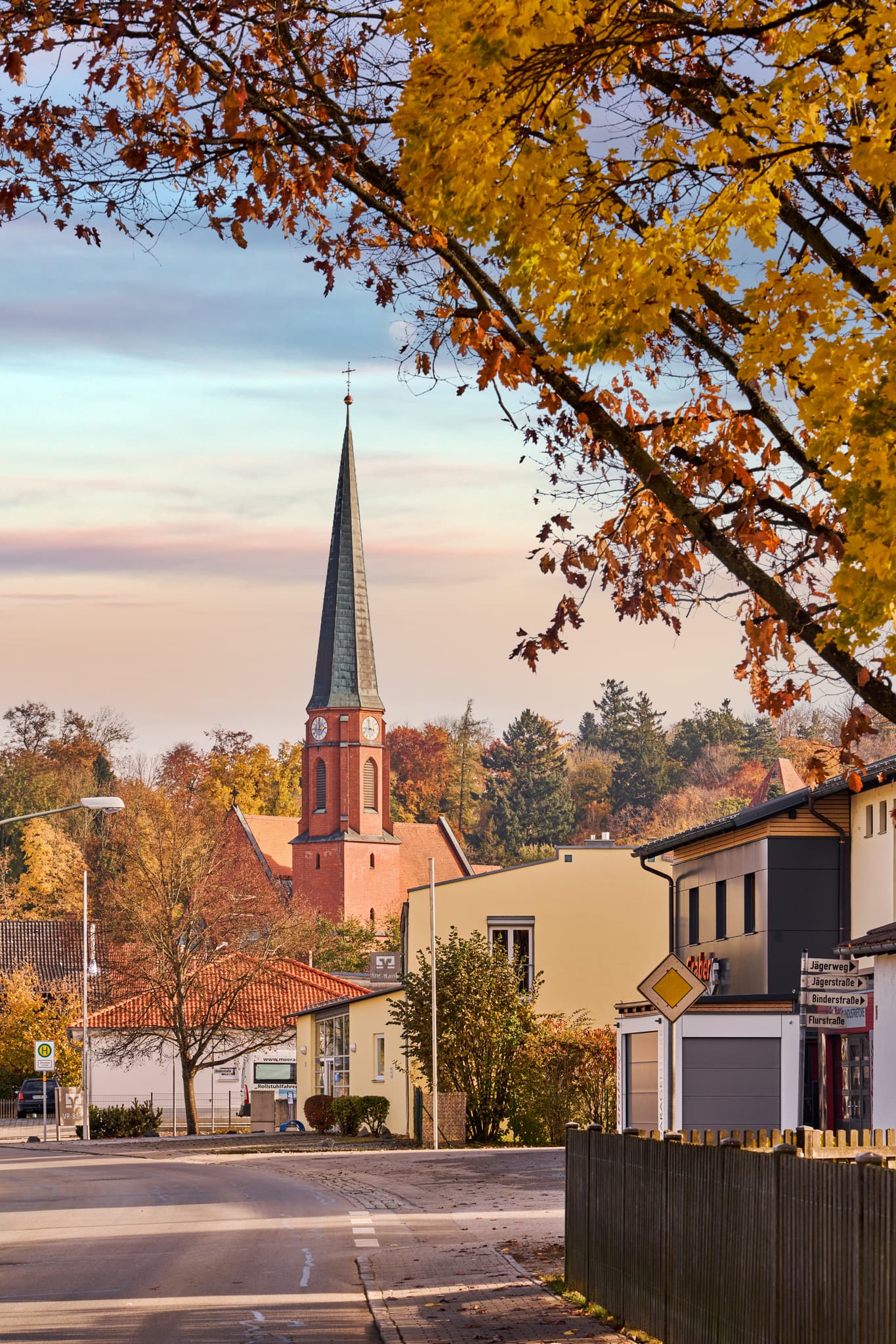 Blick auf die Dorfkirche mit markantem Turm und herbstlich gefärbten Bäumen am Hörniweg in Schönau, Landkreis Rottal-Inn, Niederbayern.