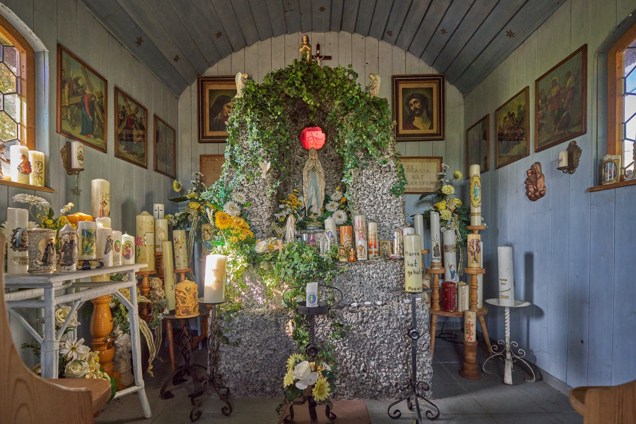 Innenansicht der Kapelle Stadlreith bei Tettenweis im Landkreis Passau, Niederbayern, Donau-Wald, Deutschland, zeigt Kerzen, Marienstatue und bunte Fenster.