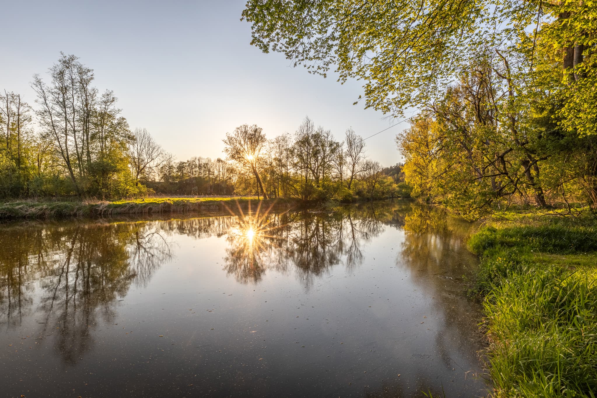 Die Isen fließt bei Aufham in Winhöring, Landkreis Altötting, Oberbayern, Inn-Salzach, Deutschland. Bäume säumen die Ufer. Die Abendsonne spiegelt sich.