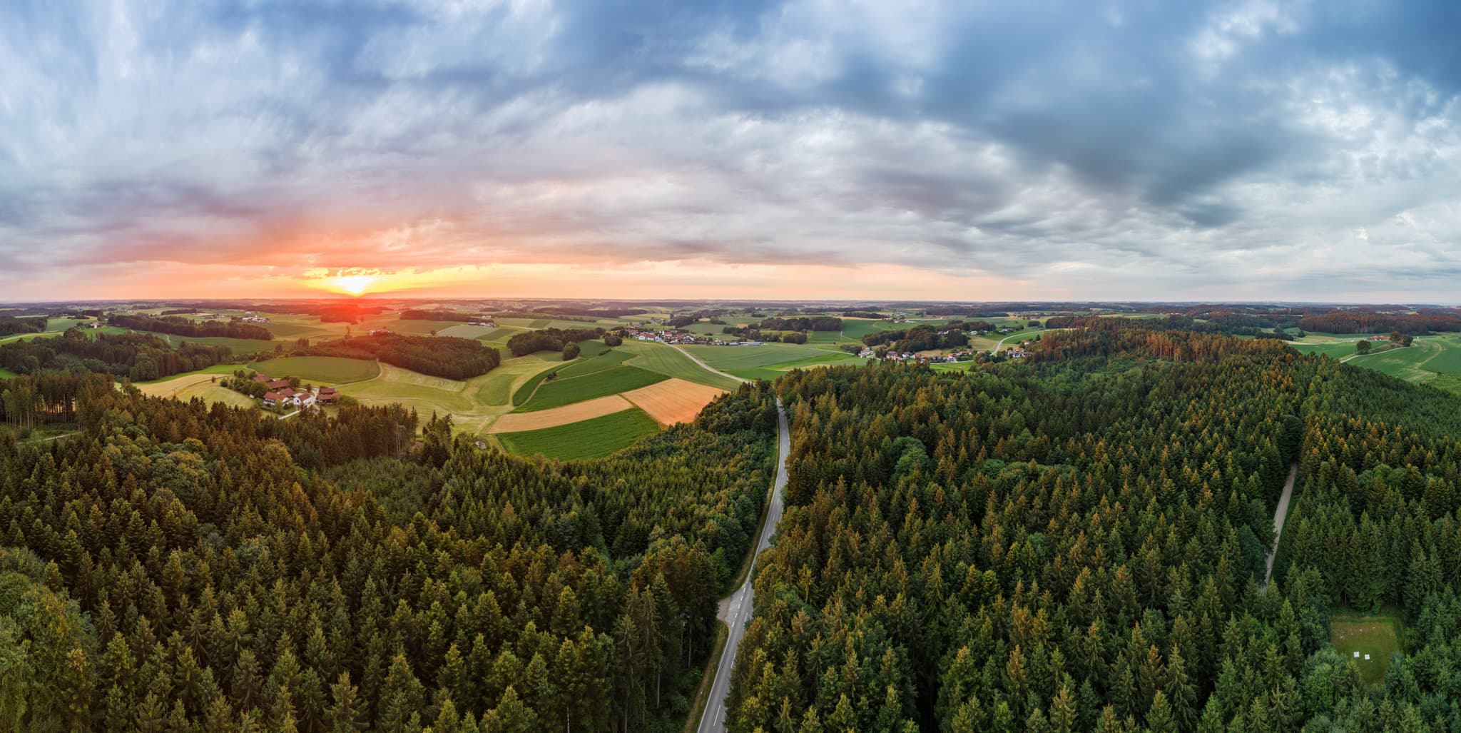 Panoramablick auf Wälder, Felder, Straße bei Reischach, Altötting, Oberbayern. Die weite Hügellandschaft des Holzlands in Deutschland erstrahlt im Abendlicht.