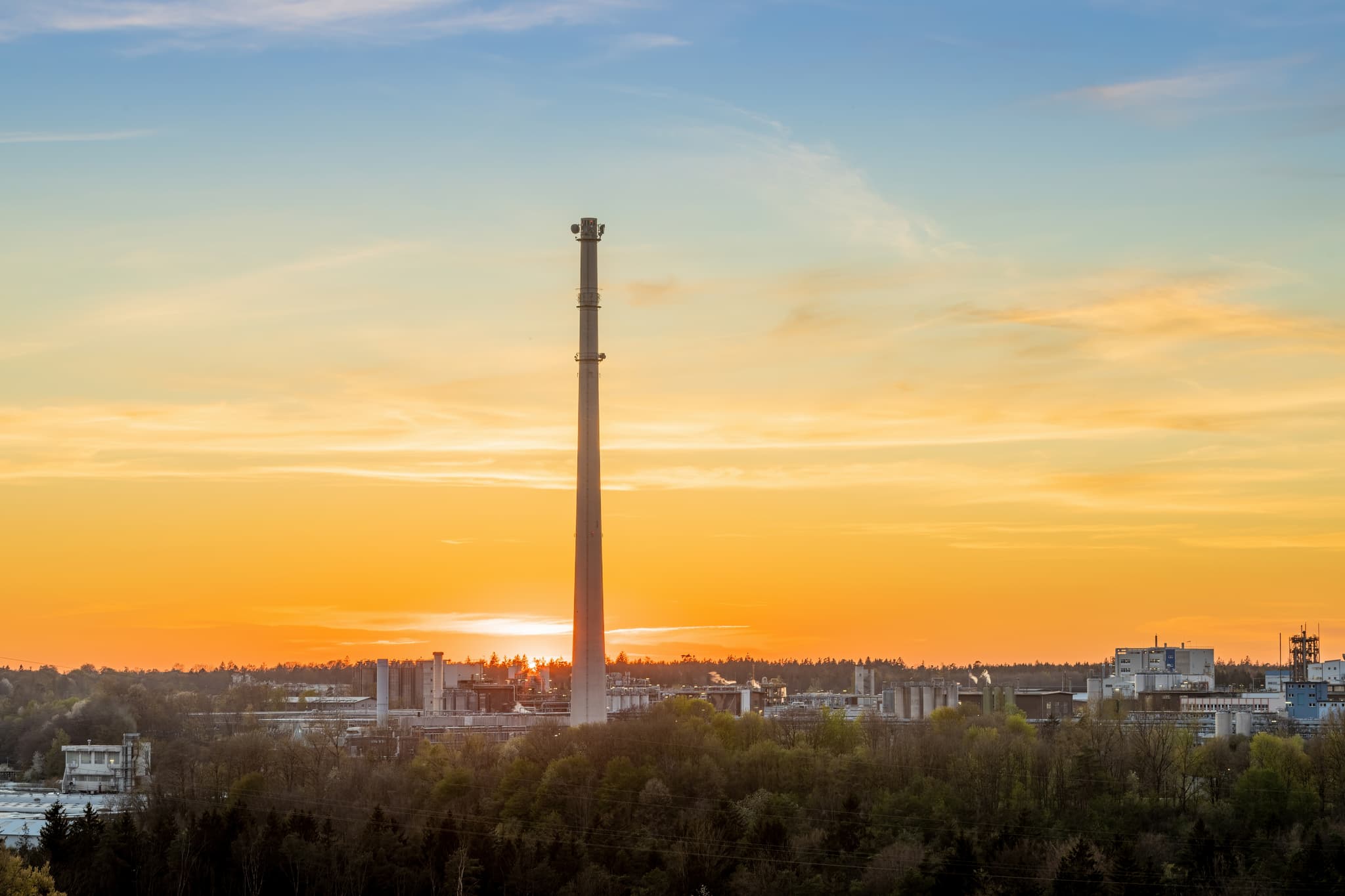Werk Gendorf, Burgkirchen, Altötting, Oberbayern. Industriegelände mit hohem Schornstein im Sonnenuntergang. Ansicht der Fabrikanlage in der Inn-Salzach Region.