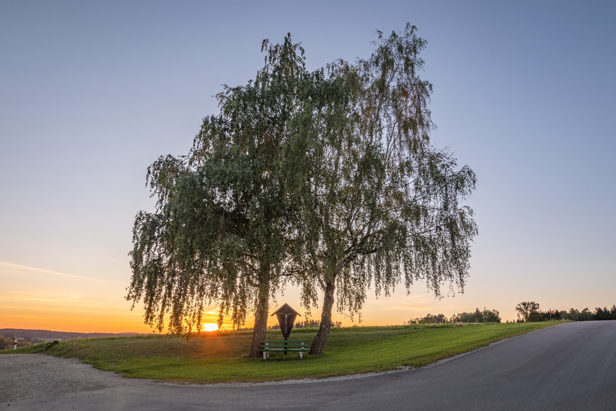 Idyllisches Wegkreuz mit 2 Bäumen bei Sonnenuntergang. Landschaft in Atzberg bei Mitterskirchen im Landkreis Rottal-Inn, Niederbayern, Deutschland