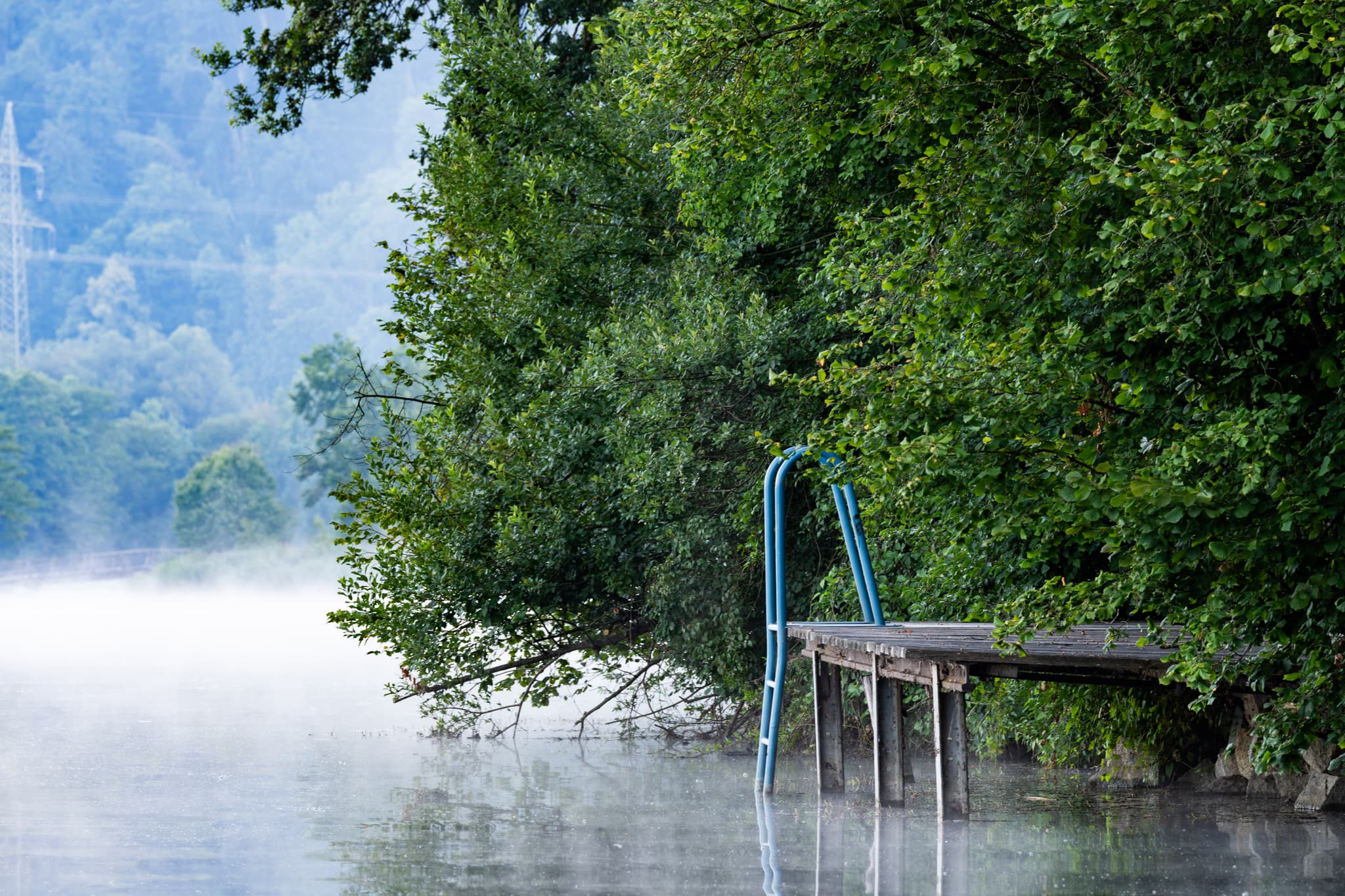 Malerischer Badesee Marktl, Altötting, Oberbayern, Deutschland. Holzsteg mit Leiter im nebelverhangenen Morgen. Idyllische Naturkulisse Inn-Salzach.