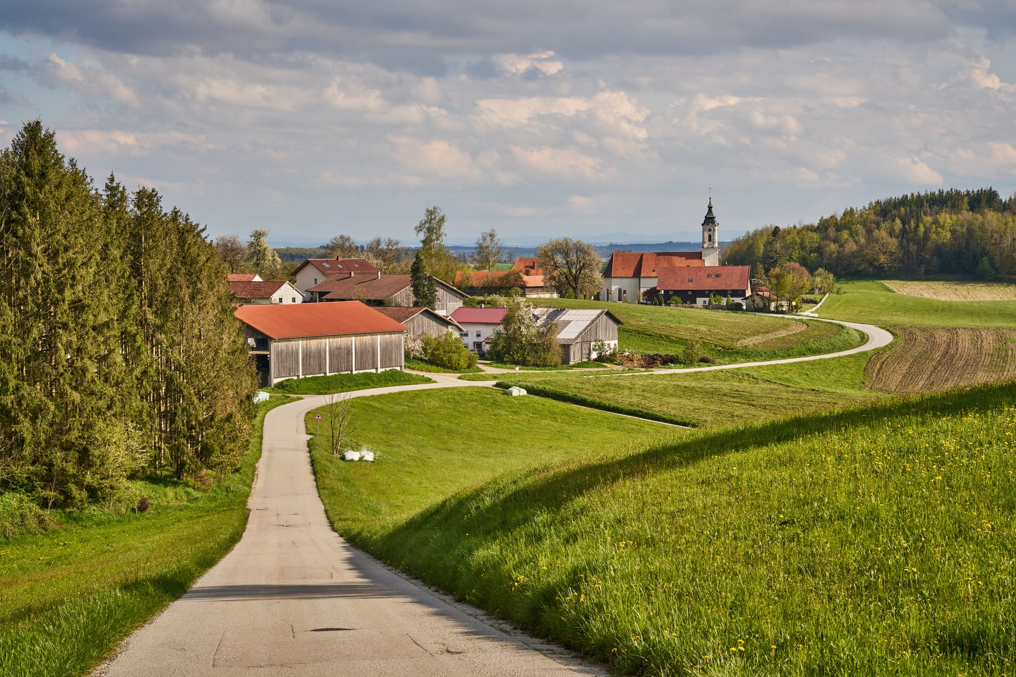 Malerisches Frühlingsbild von St. Wolfgang, Bad Griebsach, Landkreis Passau, Niederbayern, Deutschland. Zeigt Kirche, grüne Hügel, Weg im Bayerischen Wald.