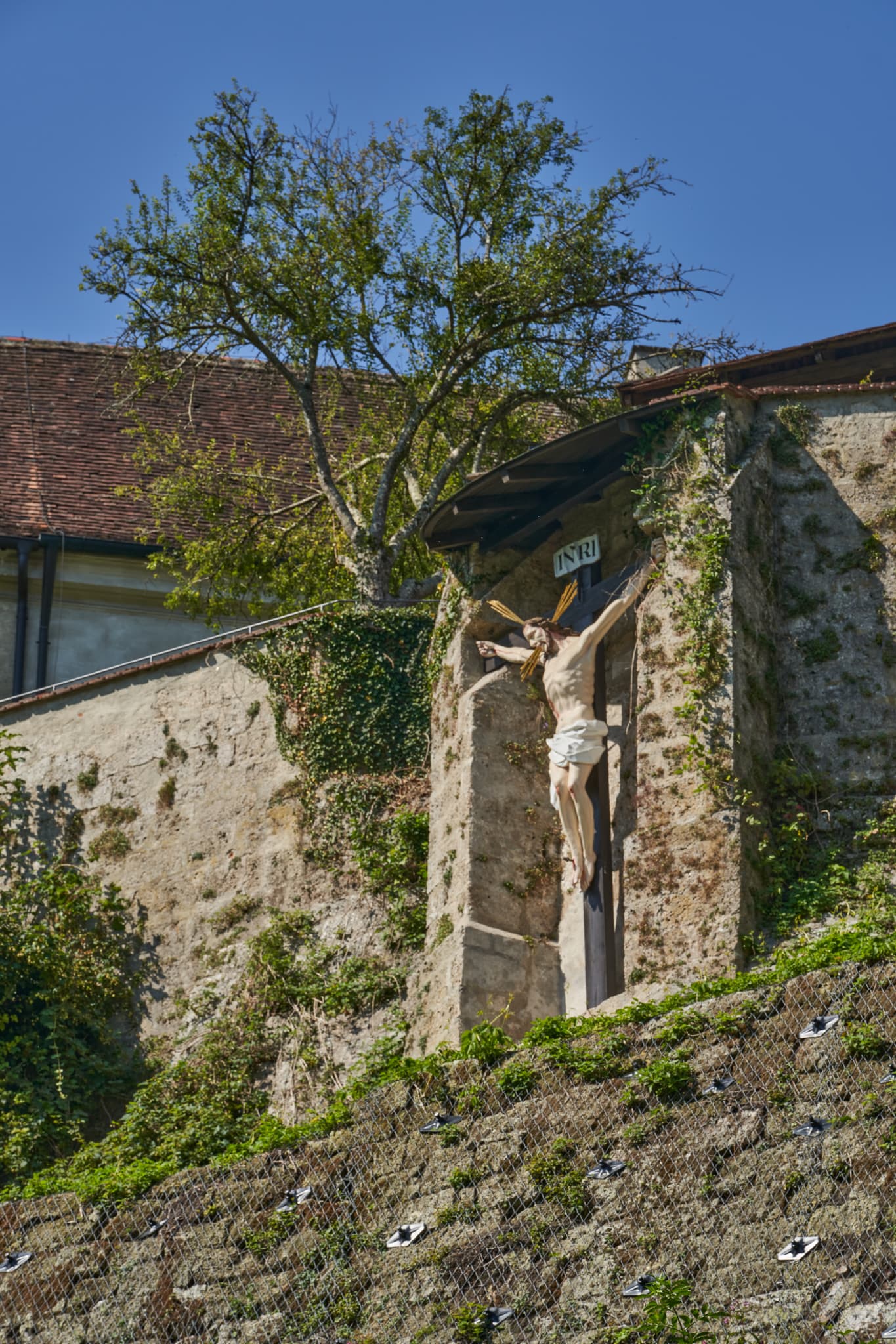 Rückseite des Klosters Raitenhaslach, Jesus am Kreuz, Burghausen, Landkreis Altötting, Oberbayern, Region Inn-Salzach. Alte Mauer mit Bepflanzung.