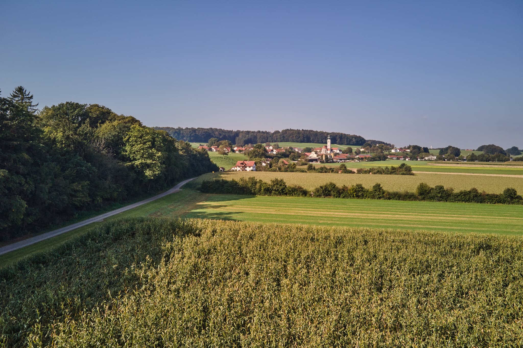 Pilgerweg Richtung Mehring bei Badhöring, Altötting, Oberbayern, Deutschland. Ländliche Szenerie mit Feldern, Straße und Dorf im Inn-Salzach-Gebiet.