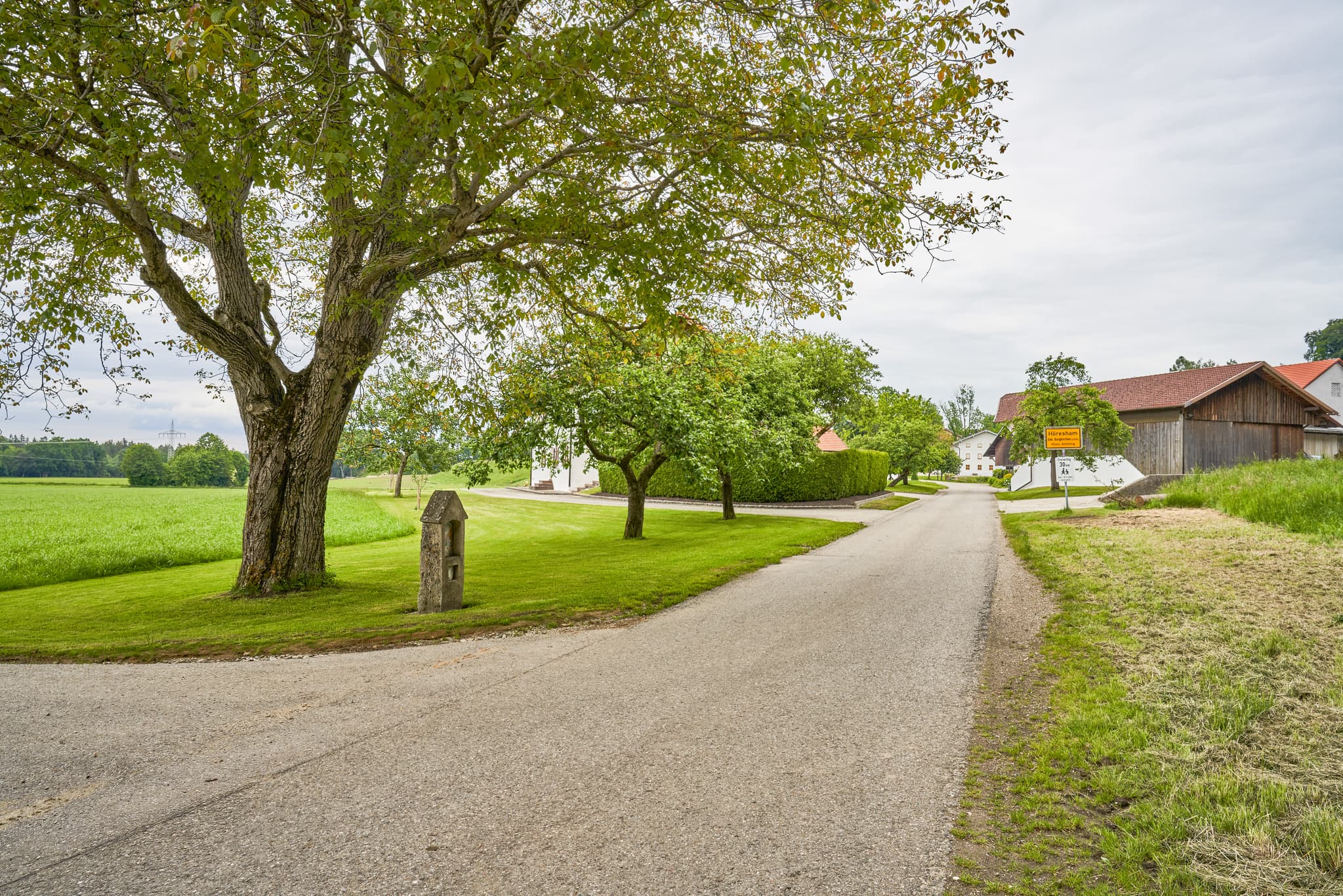 Alter Bildstock in Höresham, Burgkirchen, Altötting. Ländliche Szene in Oberbayern, Inn-Salzach, Deutschland. Zeigt Feldweg, grüne Wiesen, Bäume, Gebäude.