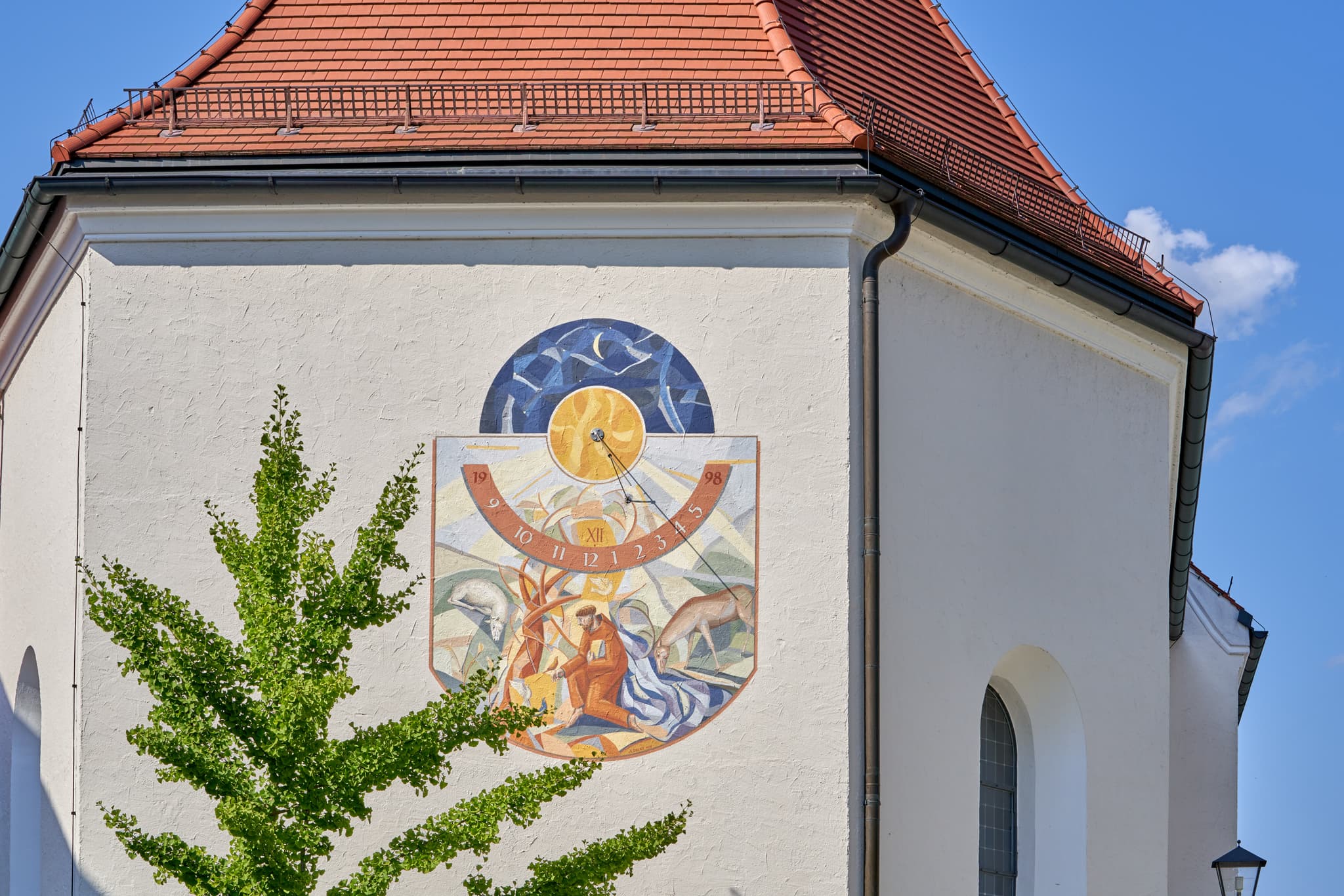 Eine kunstvolle Sonnenuhr auf der Rückseite der Bruder Konrad Kirche in Altötting. Im schönen Licht der Zeit.