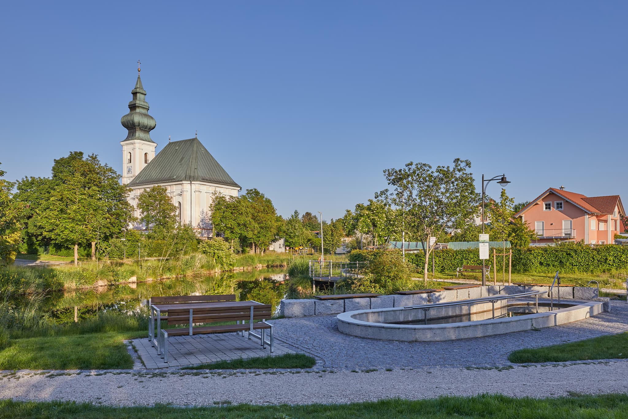 Idyllischer Dorfweiher mit Kneippanlage und Kirche in Kirchweidach, Oberbayern, Inn-Salzach, Deutschland. Genießen Sie die Ruhe und Natur.