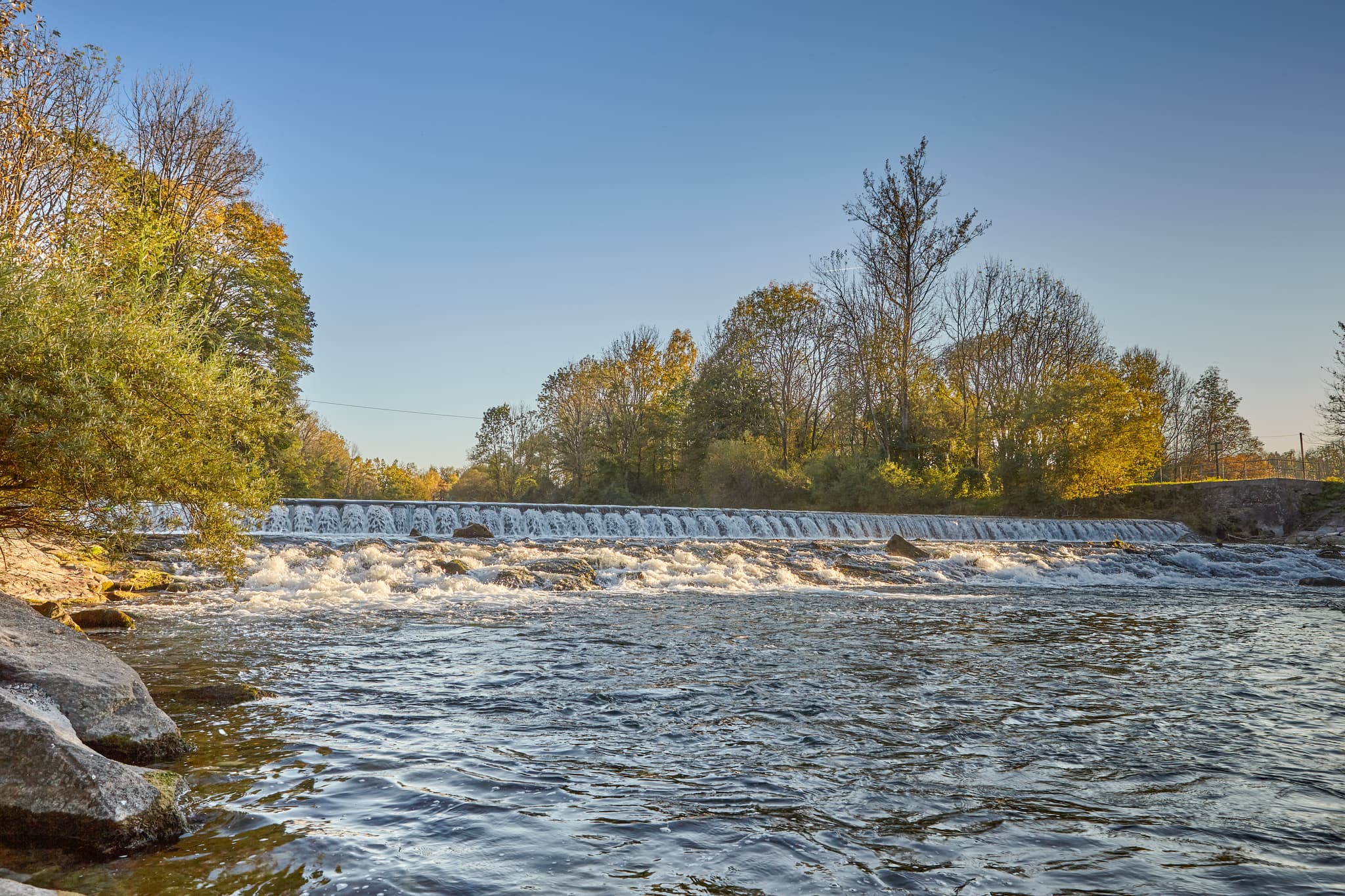 Wasserfall an der Alz in Garching, Landkreis Altötting, Oberbayern, Deutschland. Inn-Salzach Region mit herbstlicher Natur. Idyllische Flusslandschaft.