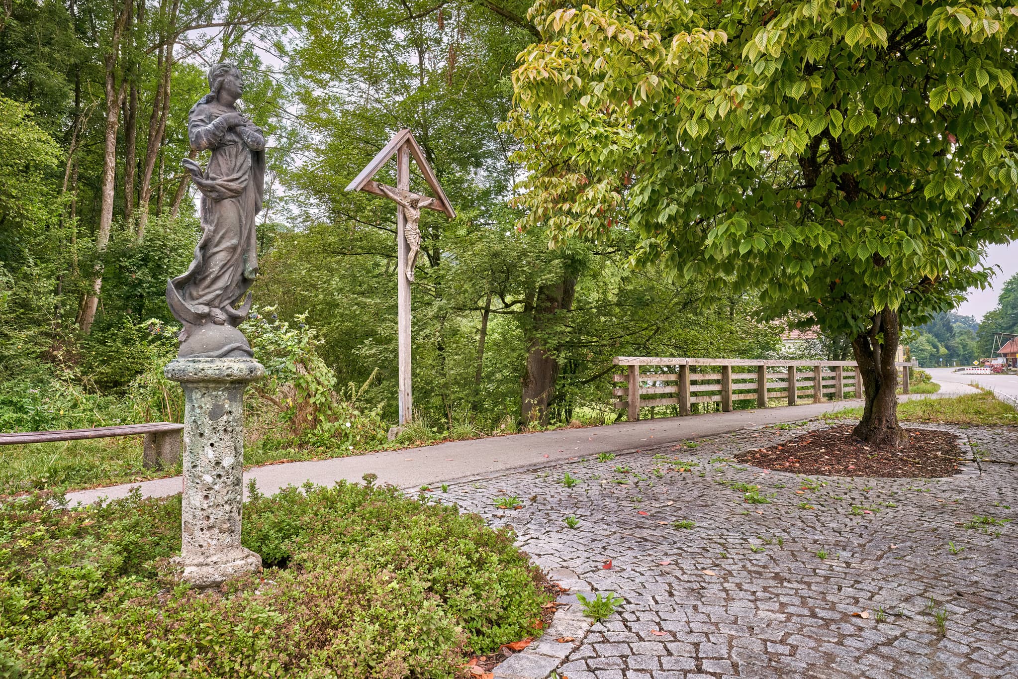 Ansicht eines Wegkreuzes und einer Mariensäule an einem gepflasterten Weg in Brandmühle, Reischach, Landkreis Altötting, Oberbayern, Inn-Salzach, Deutschland.