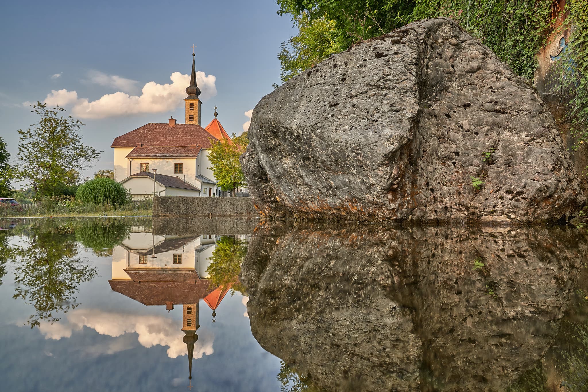 Rupertiweg Parkplatz mit Spiegelung der Kirche Maria Ach in Wanghausen mit Felsen, Hochburg-Ach, Braunau am Inn, Innviertel, Oberösterreich.