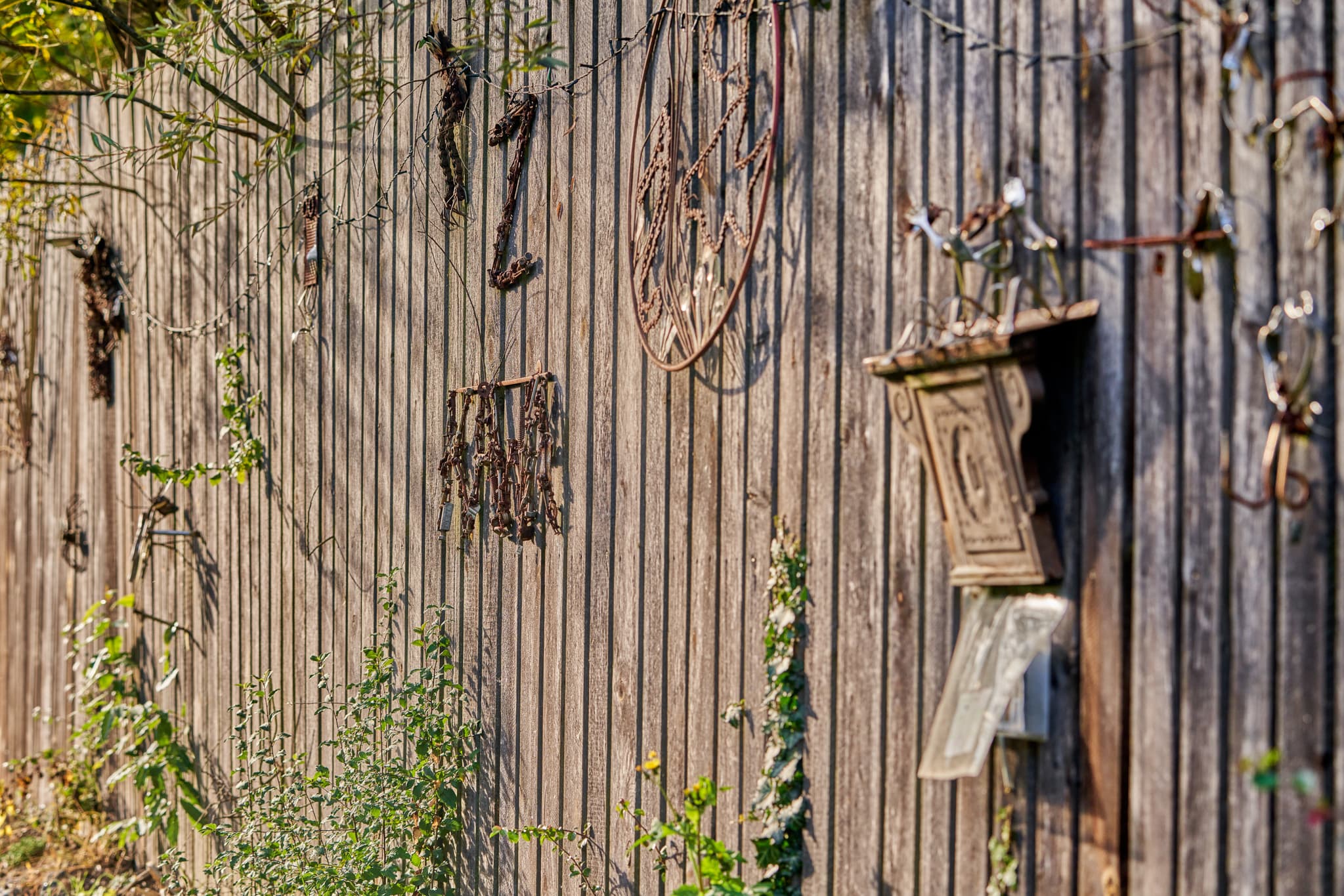 Holzzaun am Hörniweg in Schönau, Landkreis Rottal-Inn, Niederbayern. Zeigt  Metallverzierungen und Pflanzen. Hörni-Rätselweg im Bäderdreieck, Deutschland.
